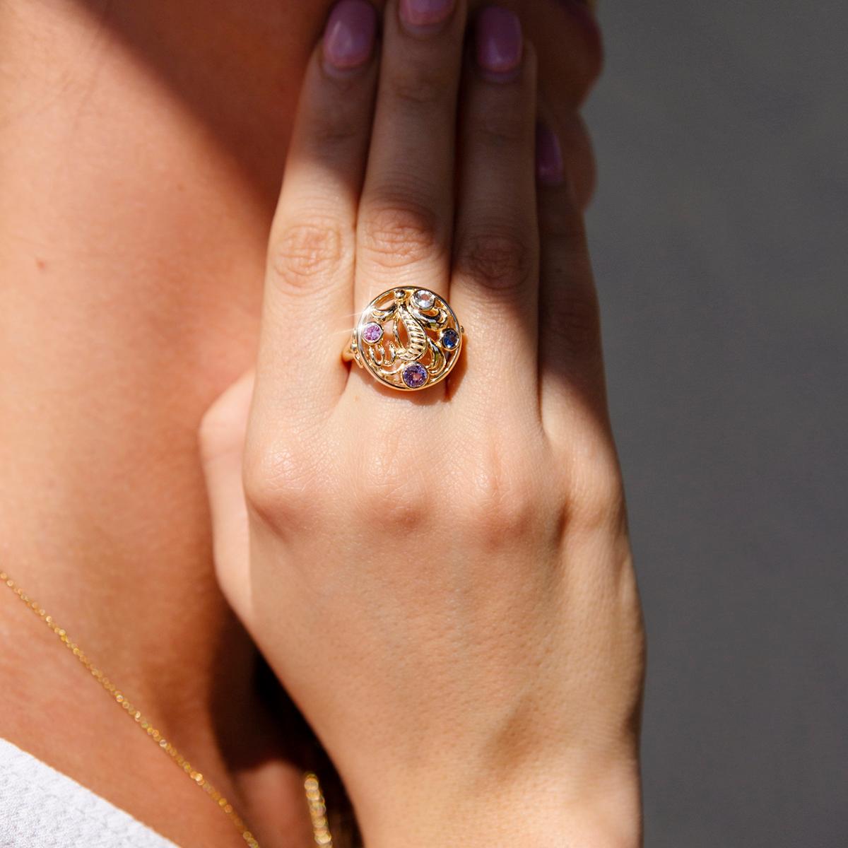 Forged in 14 carat yellow gold, this gorgeous contemporary motif ring features a diversity of wonderful natural sapphires in rub over settings resting in a gleaming and carefully designed circular motif. The featured gems are a bright purple