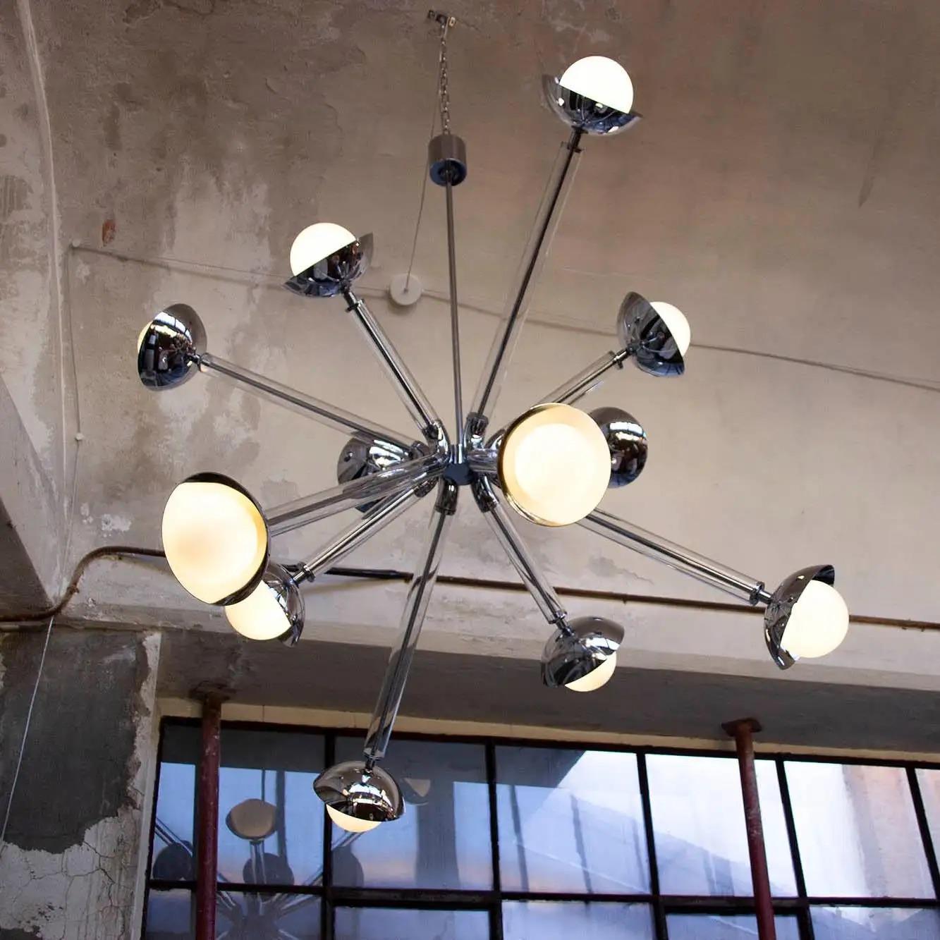 This chandelier, called Stimma, designed and entirely crafted in Italy, doesn't come from an atomic inspiration but a naturalistic interpretation. The central round core supports 12 jutting metal arms encased in transparent colored glass, ending in