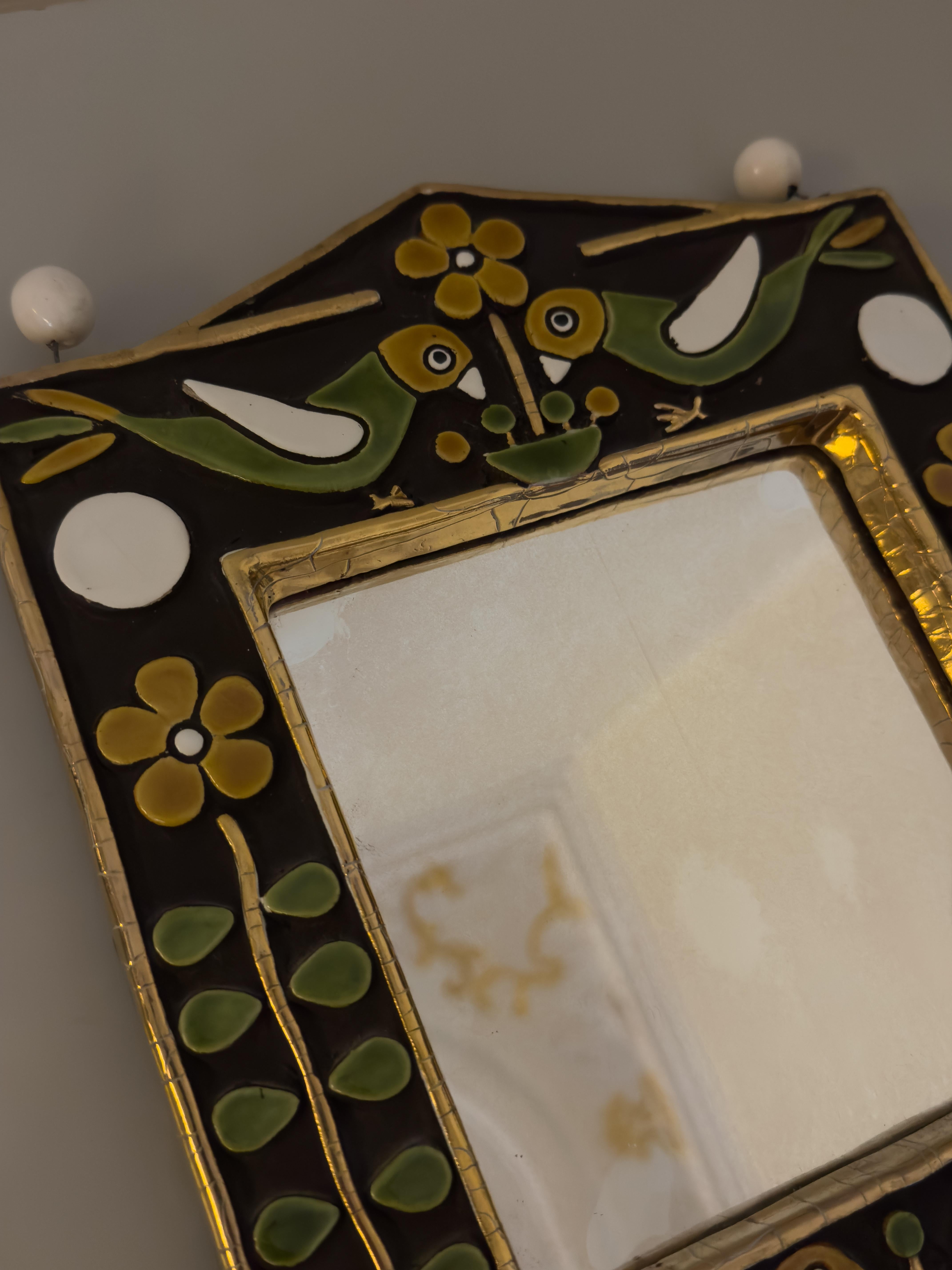 Ceramic wall mirror with birds and flowers (around the 1970s) by Mithé Espelt. A decorative piece surmounted by two pairs of enamel birds above and below the square mirror. The mirror is framed by a golden glaze that also forms the outer frame.