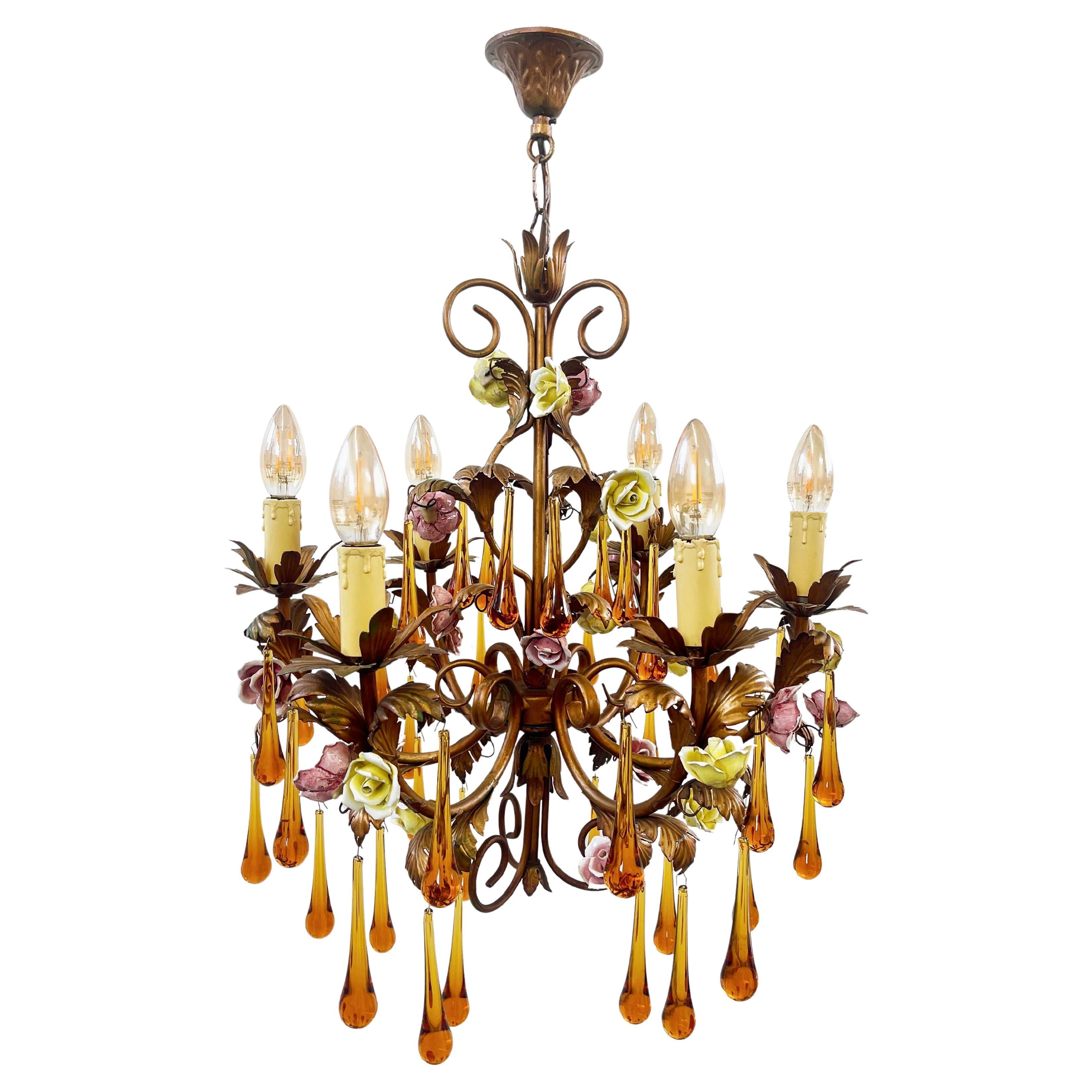 Beautifully vibrant 6-armed teardrop chandelier with Murano glass drops.
Made from Toleware with a matte copper to brass hued finish, wearing pink and yellow hand crafted rose flowers.
Vibrant dark amber glas drops, each hand made in Murano, 