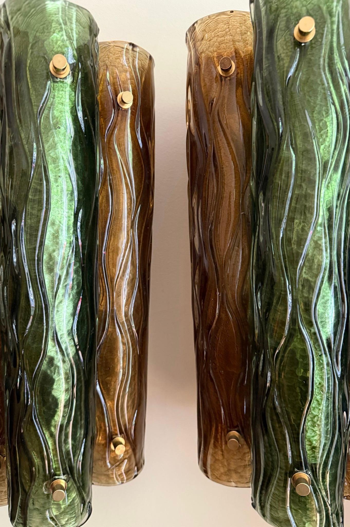 Murano glass wall lamps, composed of three vertical cylindrical shapes grouped in green and amber. The supporting structure is made of brass and is fitted with three lamp holders. Italy.

