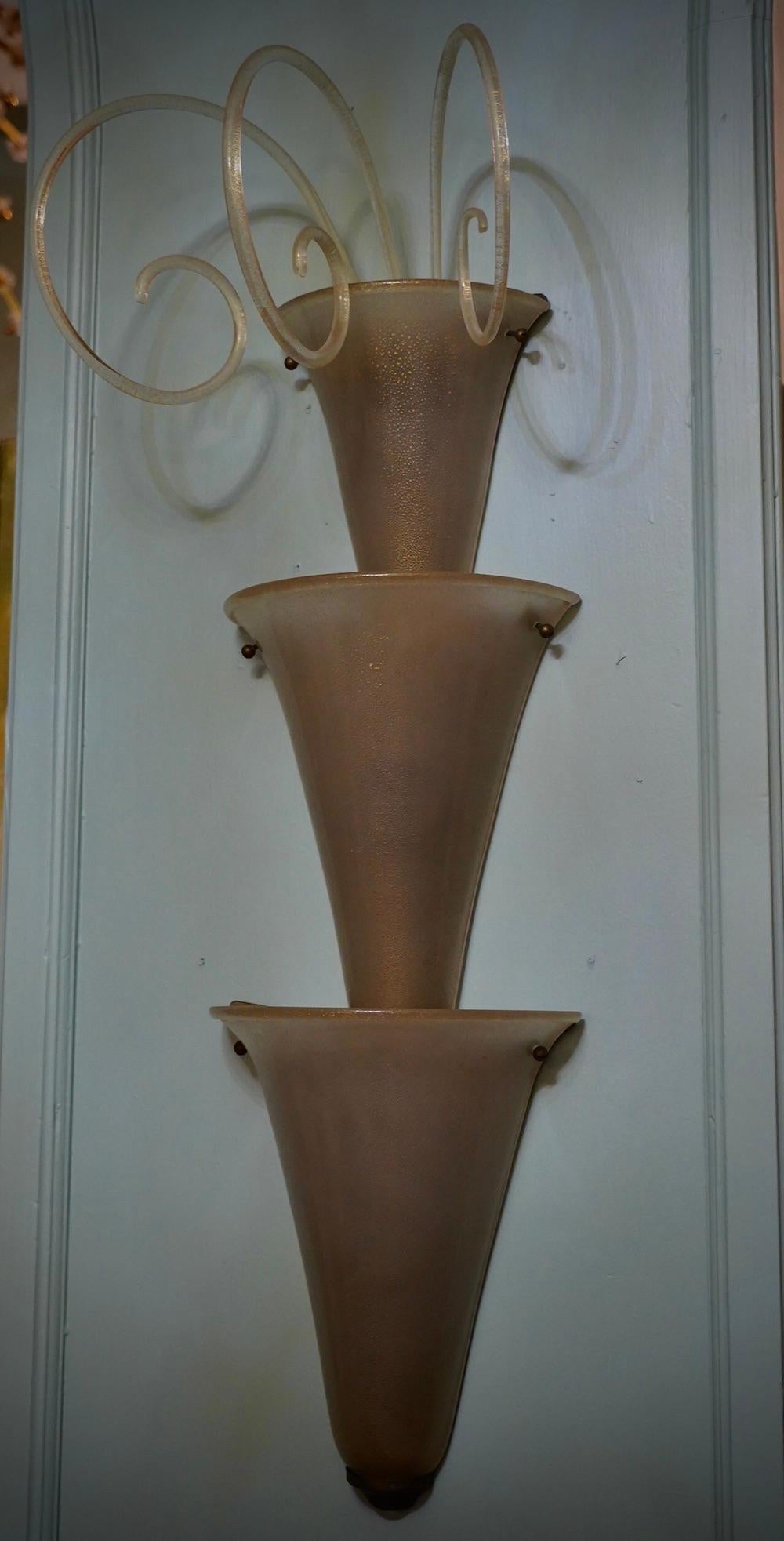 Klassische Murano-Glasapplikation. Die Öfen von Murano zeichnen sich durch ein unbestreitbar zeitloses, schlichtes und zugleich elegantes Design aus.

Die Applikation besteht aus einer Rückwand aus Messing, auf der eine Reihe von drei taubenfarbenen