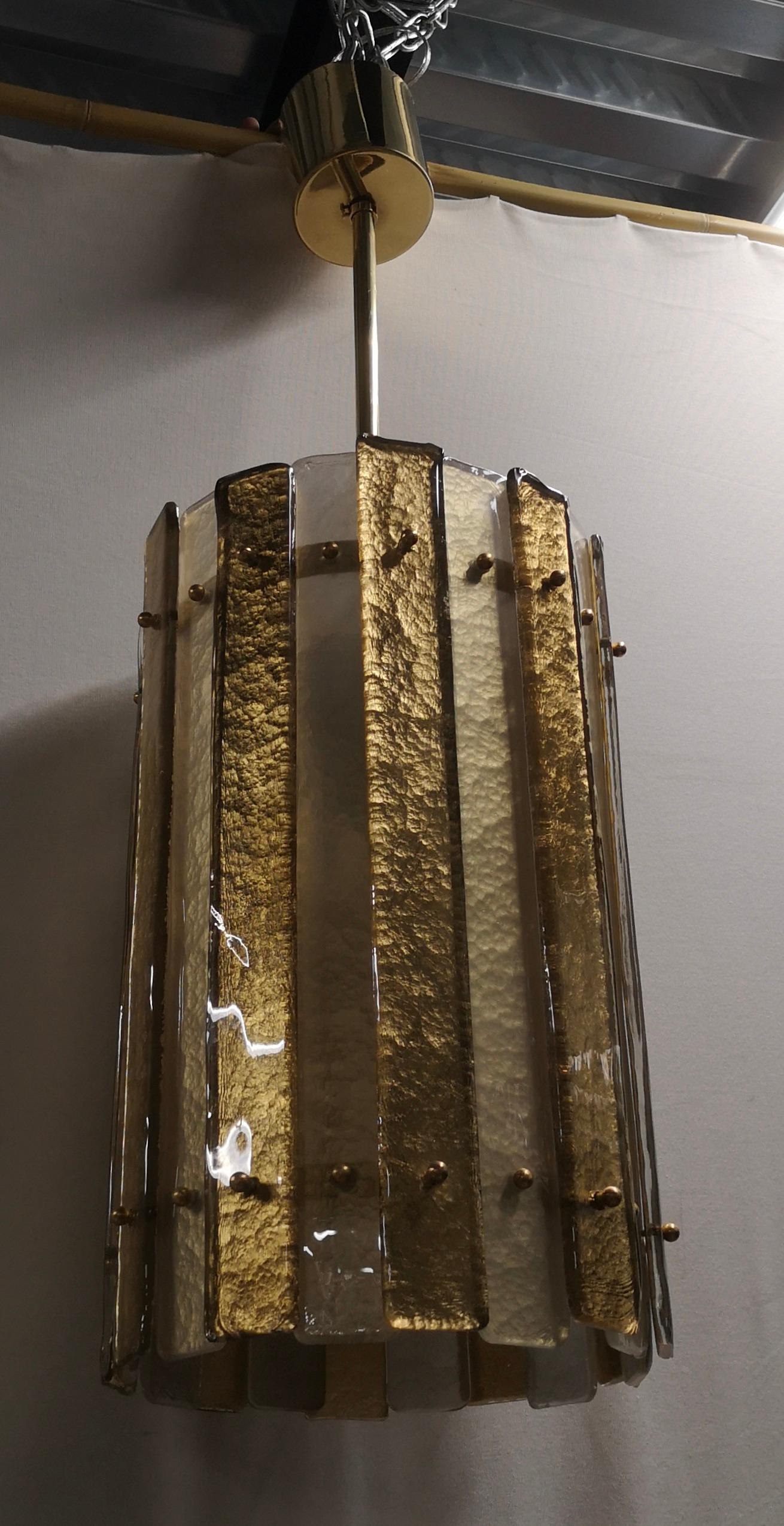 Lanterne spéciale et très originale en verre de Murano et laiton, au design unique enrichi d'un verre particulier et d'un bandeau très original.

Le lustre/lanterne a une structure cylindrique en laiton à laquelle ont été fixées de longues bandes de