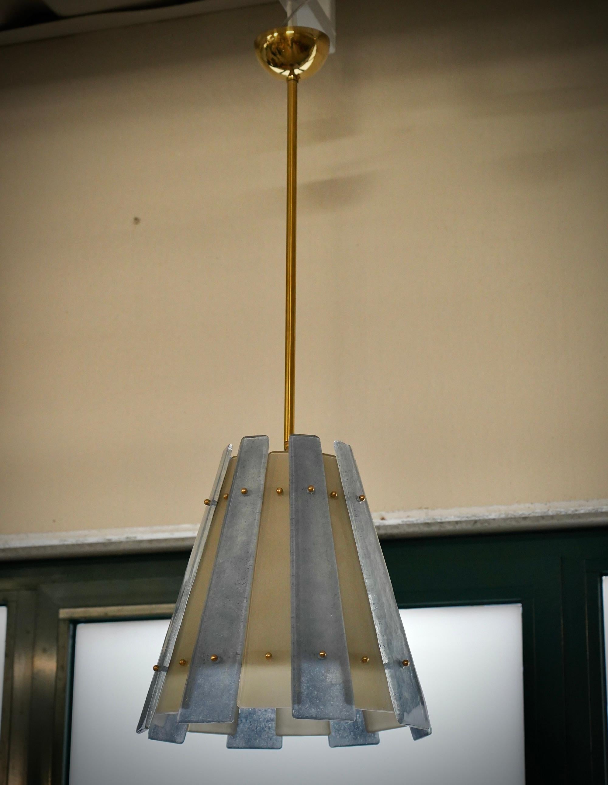 Particolare e originalissima lanterna in vetro di Murano e ottone, dal design unico arricchito da un particolare vetro con lavorazione sabbiata, dal doppio colore.

Il lampadario/lanterna ha una struttura cilindrica in ottone a cui sono state