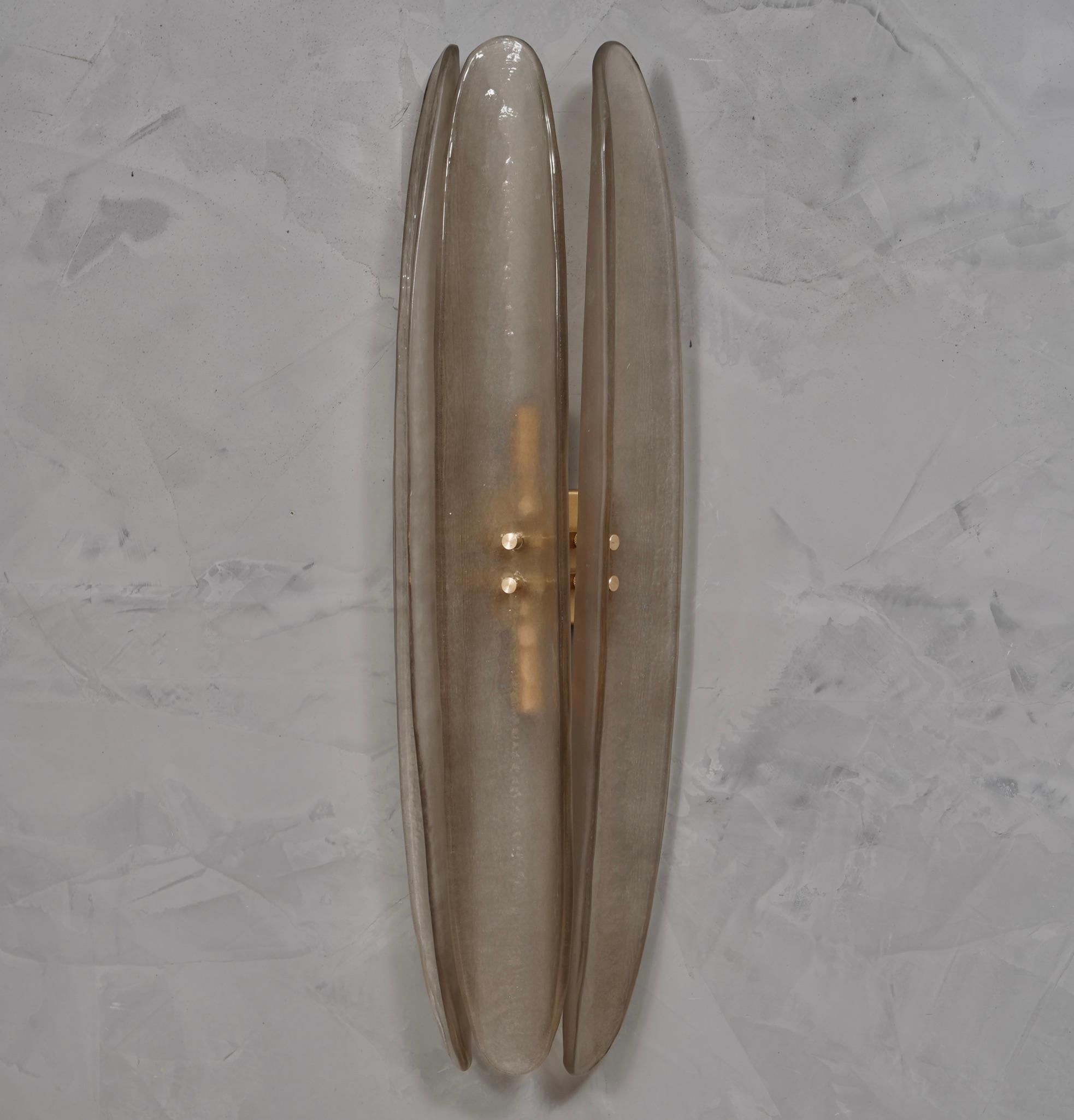 Sehr originelle Wandlampe aus Murano-Glas mit einem sehr länglichen Design des Glasblattes und einer einzigartigen rauchigen Farbe.

Die Applikation besteht aus einer goldfarbenen Metallstruktur, an der drei ganz besondere Blätter aus Murano-Glas