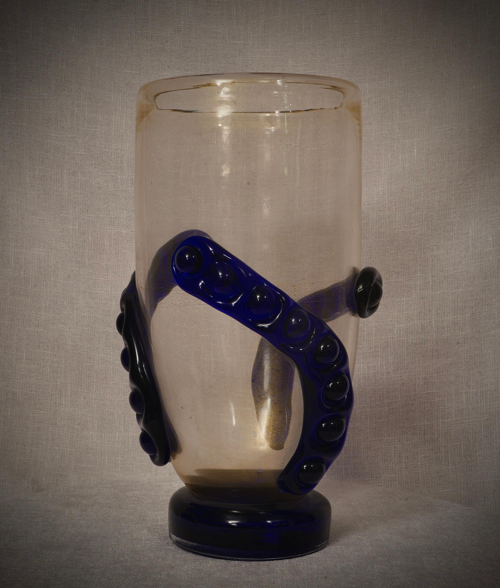 Espléndido jarrón de cristal de Murano. Observa las preciosas trenzas azules aplicadas en caliente al cuerpo del jarrón dorado. Un magnífico color dorado con trenzas azules. Los hornos Murano crean un diseño innegablemente atemporal, sencillo pero