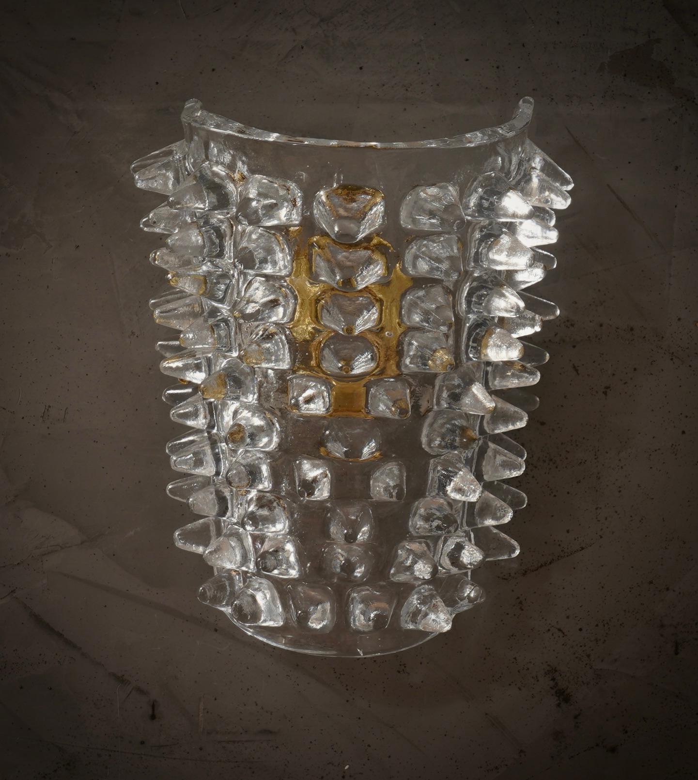 Este aplique de cristal de Murano transparente presenta un diseño refinado y delicado.

El aplique presenta una estructura de latón que alberga un espléndido azulejo de rostra de cristal de Murano transparente. El diseño es muy limpio y sencillo,