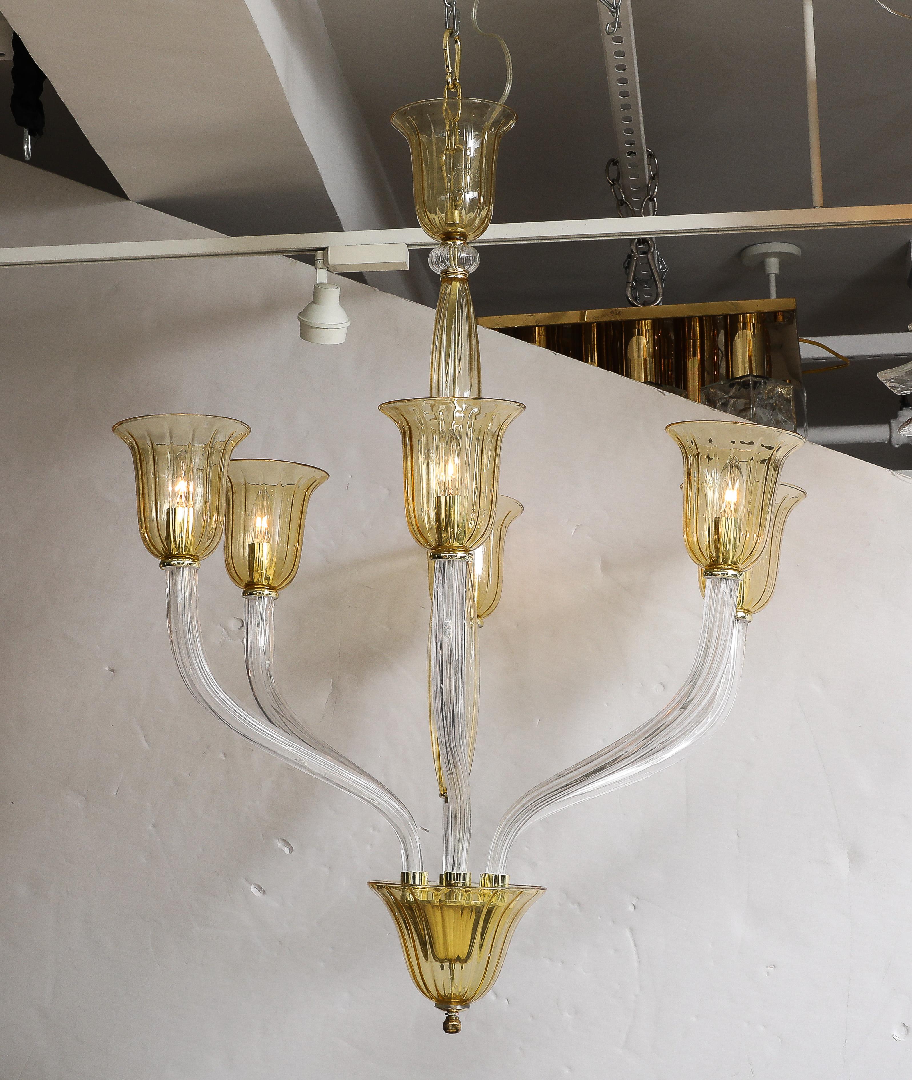 Lustre à 6 bras en verre d'art de Murano soufflé à la main avec des bras cannelés clairs et des accents en verre ambré/miel. Câblée pour une utilisation aux États-Unis, elle utilise des ampoules de type candélabre de 15 à 40 W. 