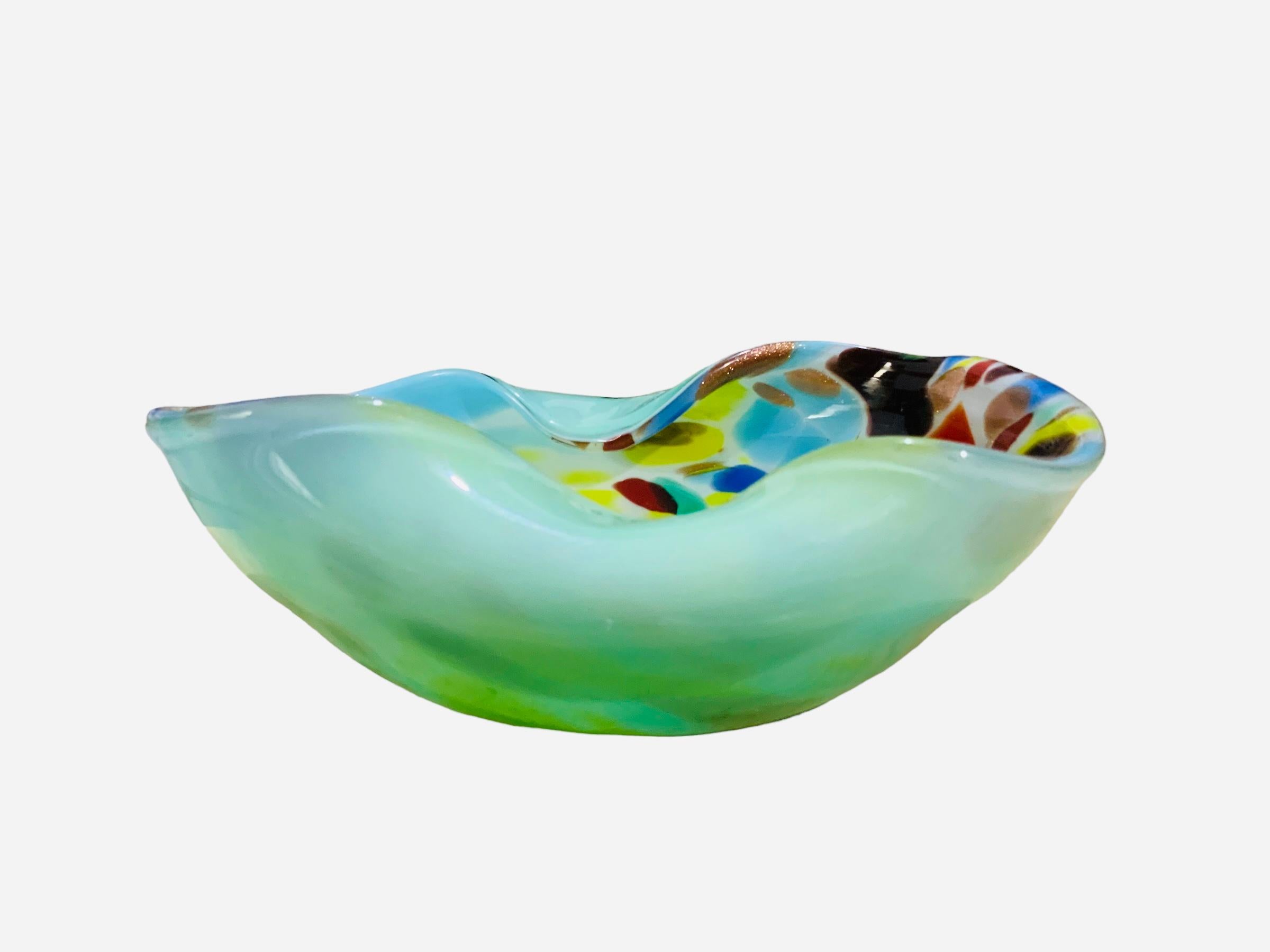 This is a Fratelli Toso Murano Art Glass Confetti ashtray. It depicts a round glass bowl folded in two sides. It is mint green in the back and in the front is very colorful with confetti asymmetrical geometric figures.