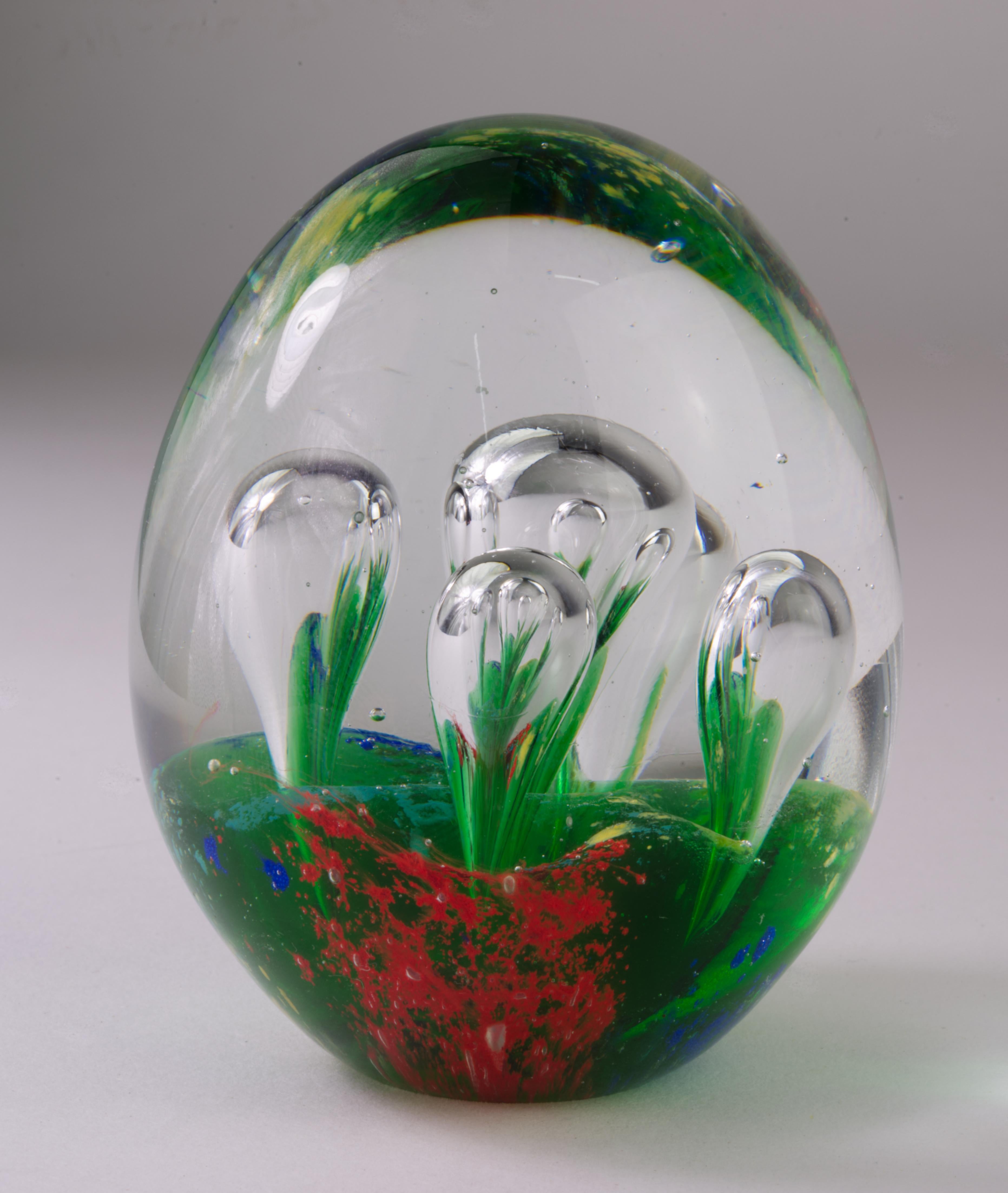  Elongated Murano art glass paperweight with large controlled bubbles forming an abstract biomorphic shaped element within the piece is handmade with central gather of green glass and blue, red, and yellow pigments encased in clear glass.

