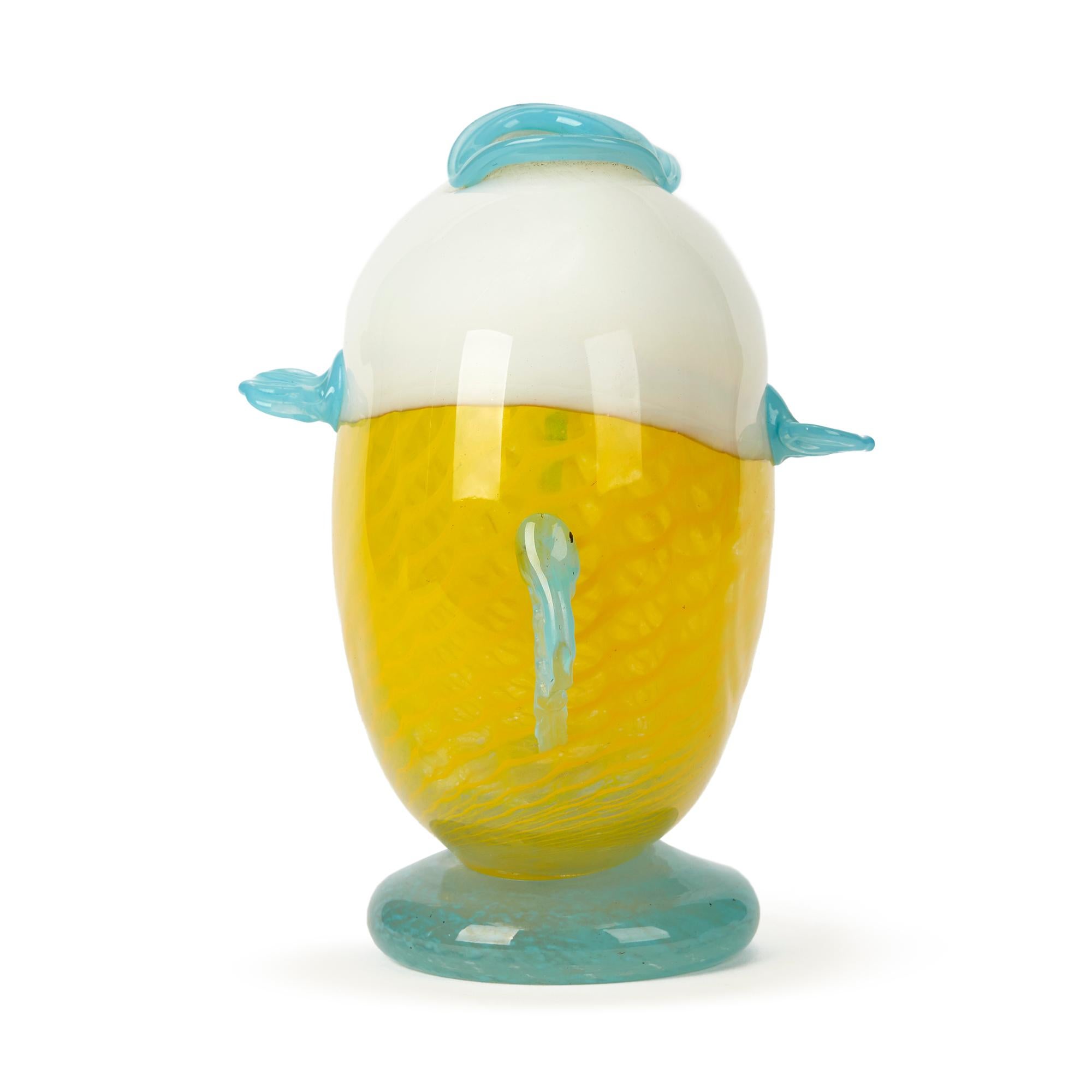 Un insolito vaso in vetro artistico attribuito a Murano, modellato come un pesce palla. Il vaso ha un corpo piatto e arrotondato in vetro bianco e giallo a squame con occhi applicati e pinne e labbra in vetro blu che formano la parte superiore del