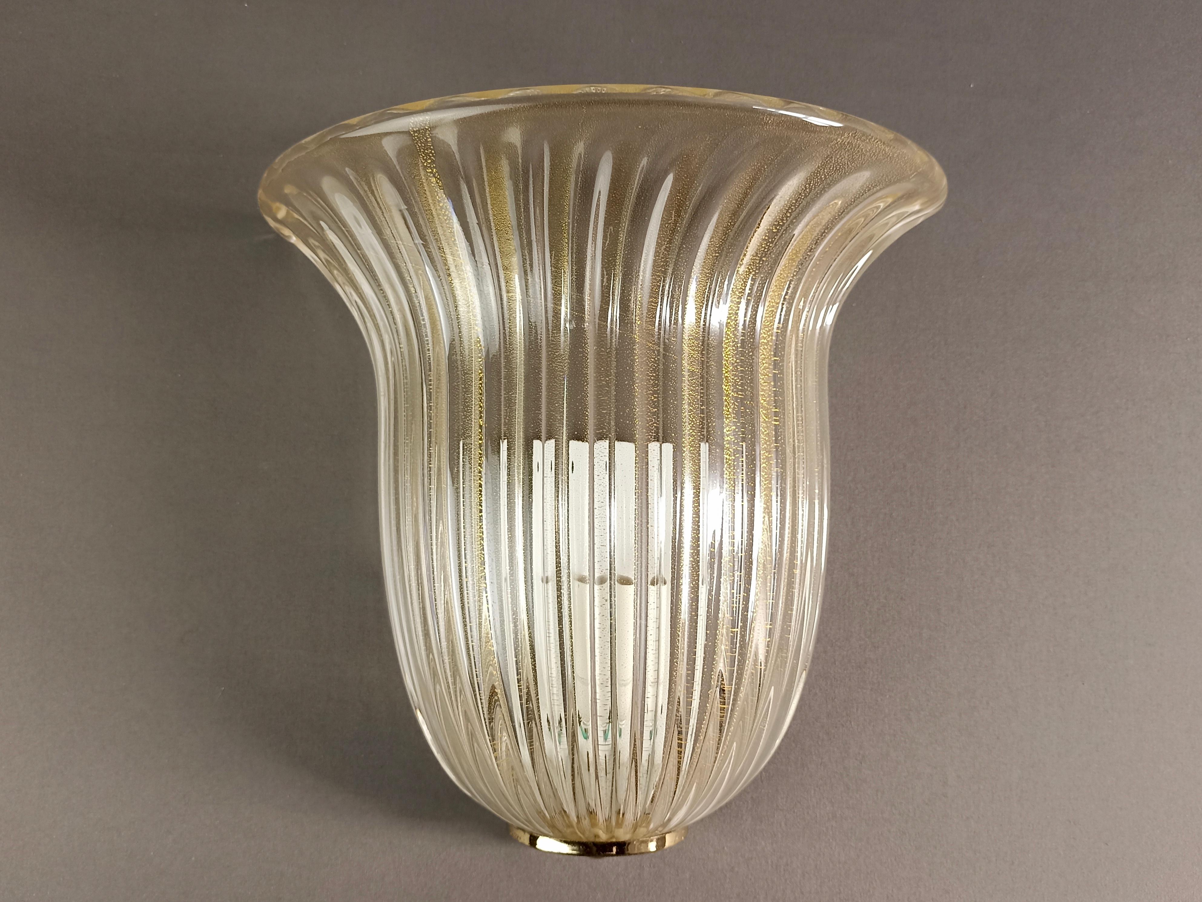 Beautiful single wall lamp from the 1980s made of clear Murano glass with gold inclusions, wonderful ribbed work, great style.
The lamp is fixed to the wall with a white lacquered metal base.
This is a truly refined and timeless object, which fits