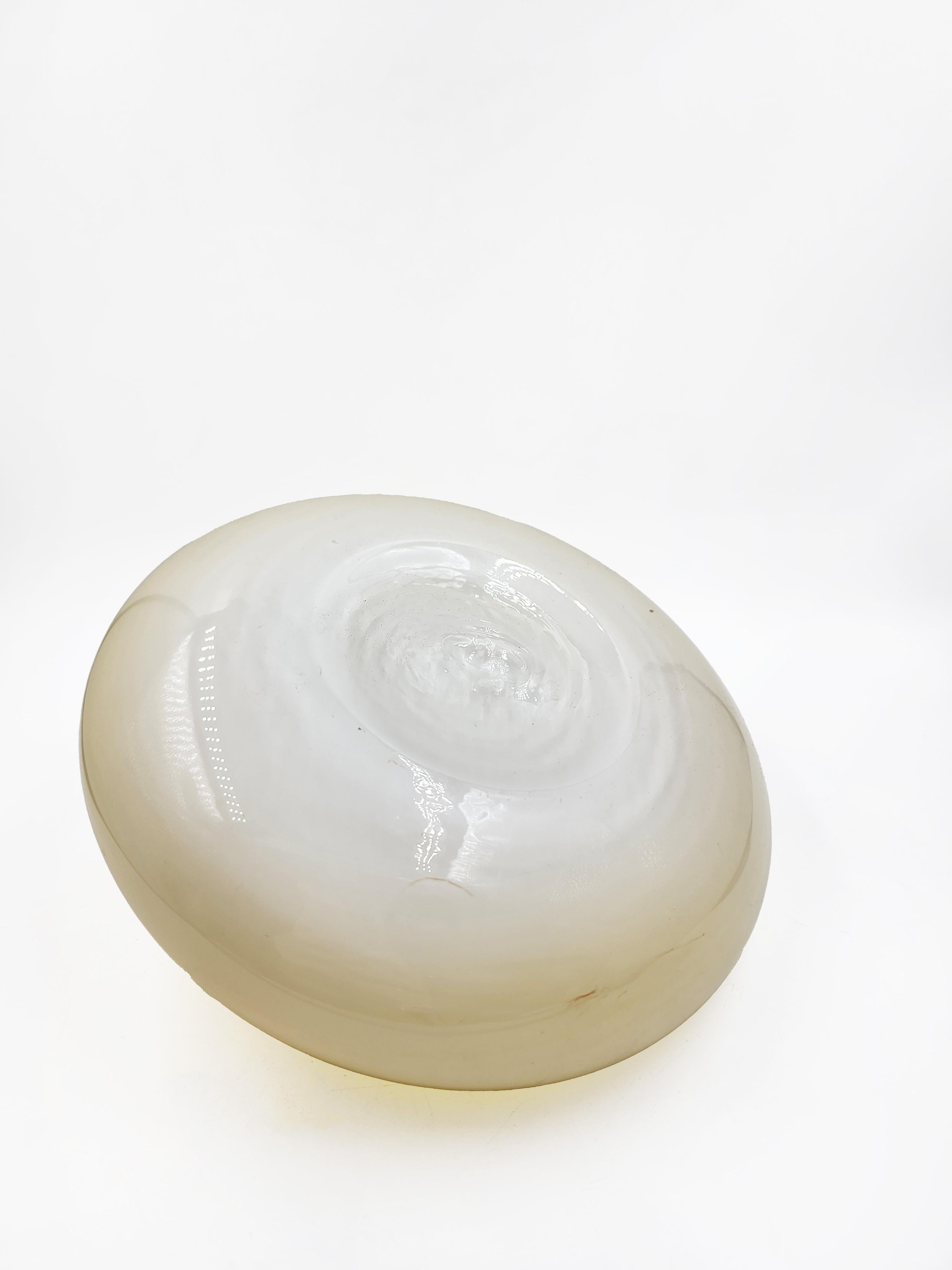 Murano Art Glass Centerpiece
This glass centerpiece features a flattened oval shape, with a small opening at the top. The two-tone design combines an opaque glass base in a beige or cream hue, which gradually blends into a transparent glass top