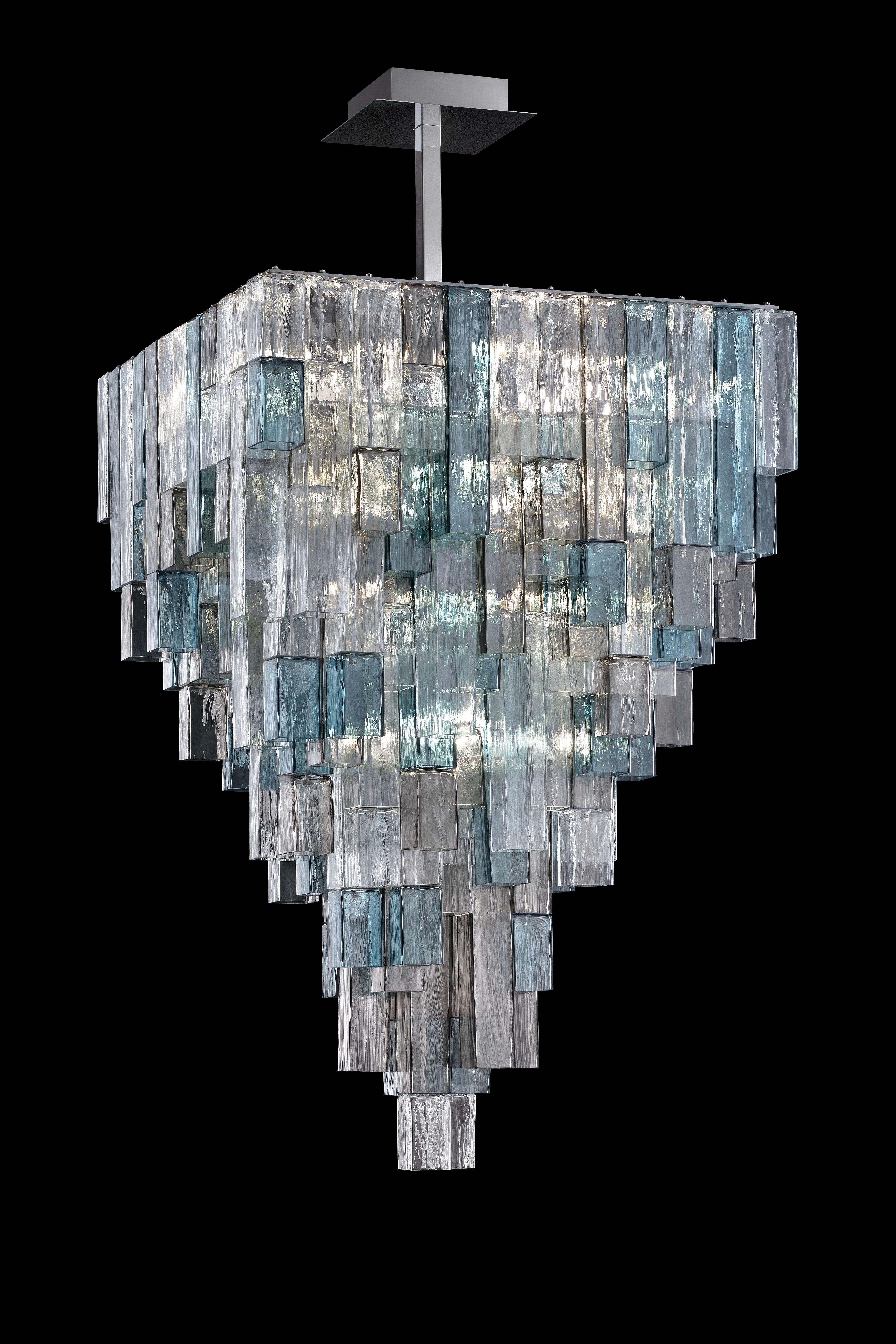 Forcefully three-dimensional, these pieces interact with the architecture of spaces, defining volumes and boundaries. The structure of the lamps is completely concealed, while tubes with a square cross-section descend from the ceiling. The