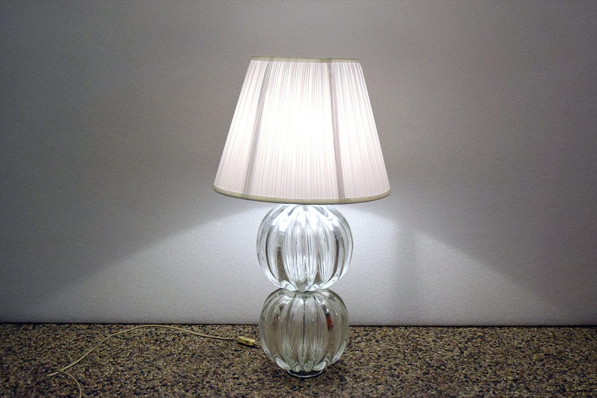 1970s Murano blown glass table lamp.
Base composed of two overlapping spheres of blown and ribbed glass, chrome-plated metal foot and joints, pleated fabric shade.
In excellent condition.
Glass diam 25 cm - lampshade ca 35-40 cm
Modifica