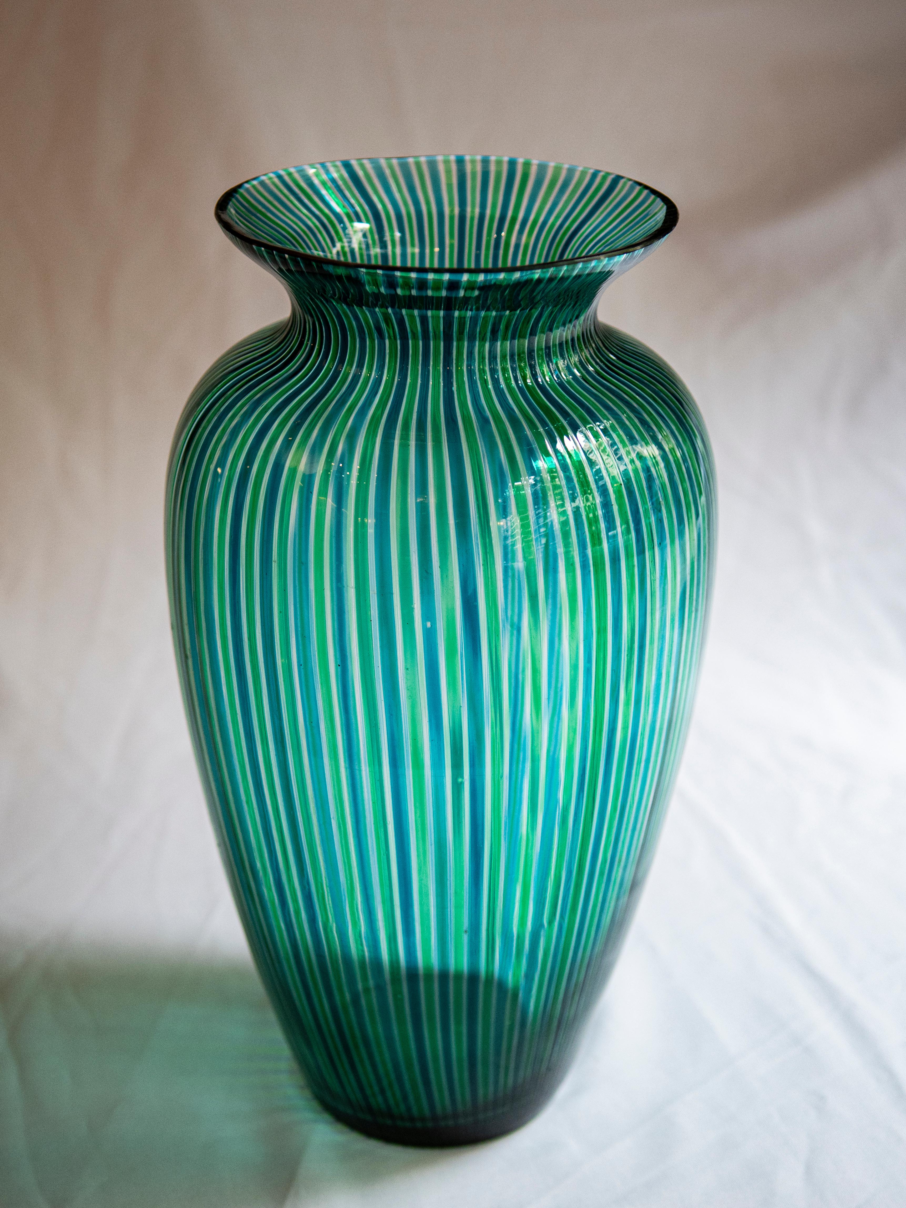 
Step into the realm of timeless elegance with this exquisite Murano blown glass vase, attributed to the renowned designer Gio Ponti and dating back to the 1960s. Adorned with enchanting green and blue vertical stripes, it stands as a testament to