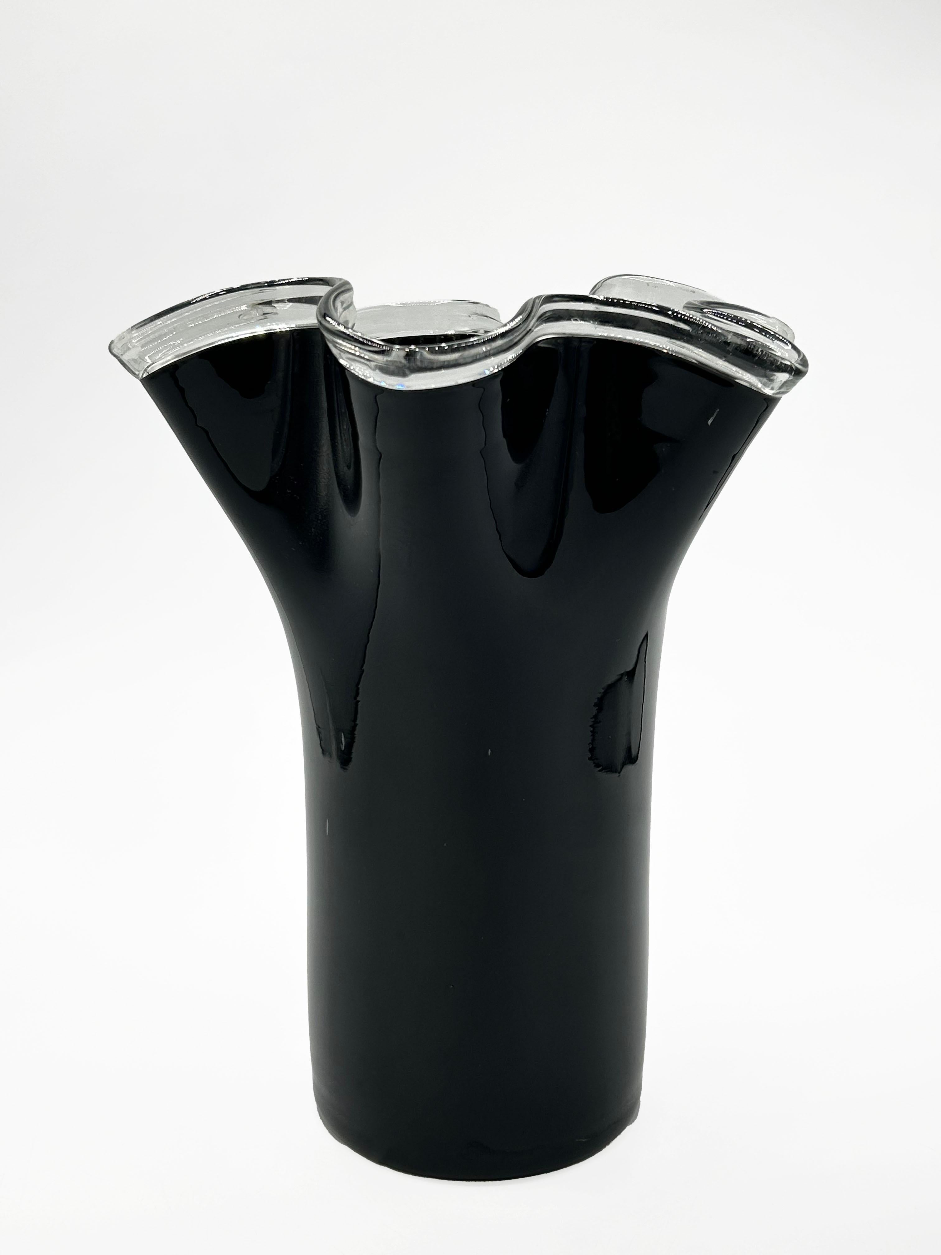Murano Blown Glass Vase circa 1950s
This blown glass vase, likely from the 1950s, features an opaque black glass body with a distinctive wavy top edge in clear glass. Its design blends a cylindrical base with a sculptural opening, creating a sober