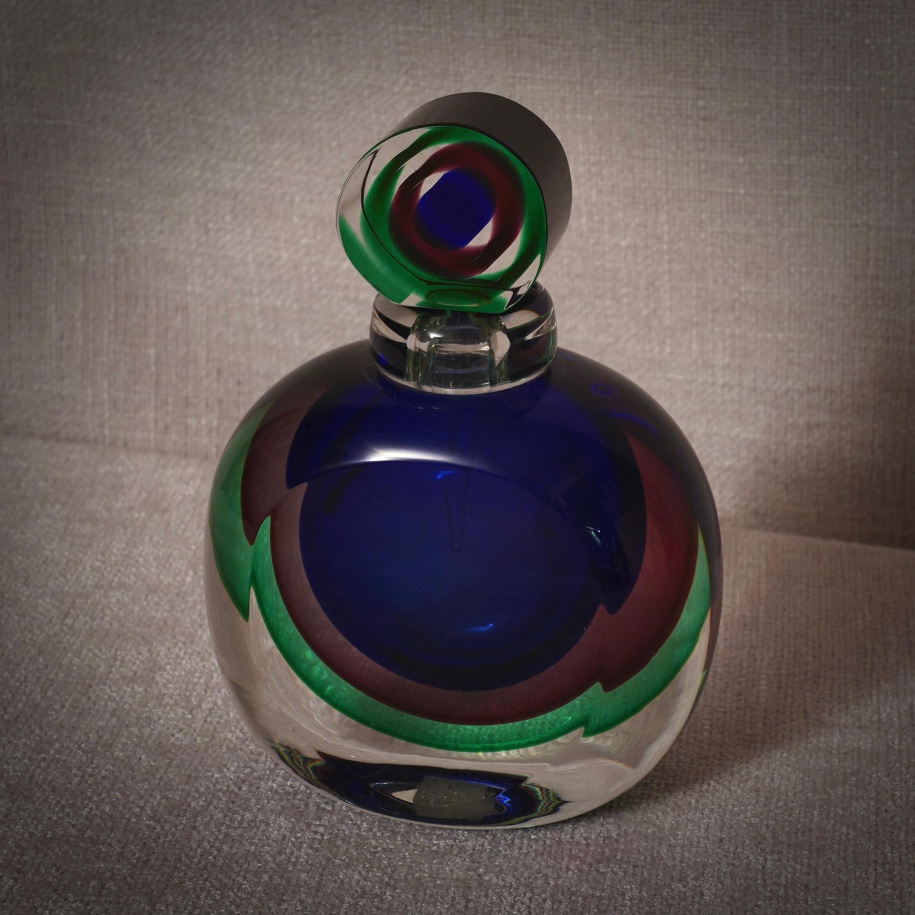 Ein Parfümflakon mit Innenverzierungen in verschiedenen Blau-, Grün- und Transparenttönen. Eine Skulptur von höchster Qualität, ein Unikat aus Murano.

Der Parfümflakon, ein Klassiker der Murano-Glasbläserei, ist in Murano nach wie vor ein