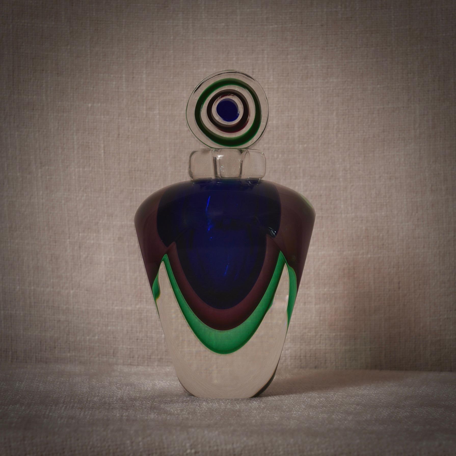 Ein Parfümflakon mit Innenverzierungen in verschiedenen Blau-, Grün- und Transparenttönen. Eine Skulptur von höchster Qualität, ein Unikat aus Murano.

Der Parfümflakon, ein Klassiker der Murano-Glasbläserei, ist in Murano nach wie vor ein