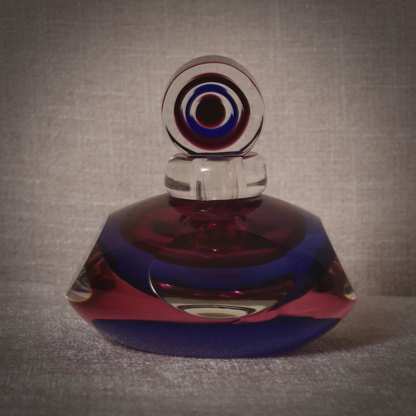 Ein Parfümflakon mit Innenverzierungen in verschiedenen Blau-, Rosa- und Transparent-Tönen. Eine Skulptur von höchster Qualität, ein Unikat aus Murano.

Der Parfümflakon, ein Klassiker der Murano-Glasbläserei, ist in Murano nach wie vor ein