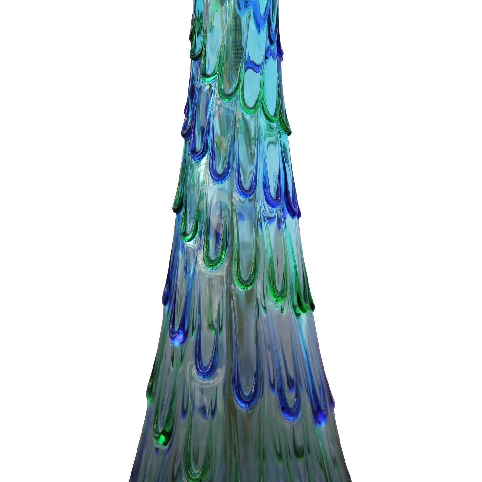 Beautiful blue glass table lamp with blue and green drip. The lamp has a brass base with a felted bottom. Comes with a tan lamp shade.