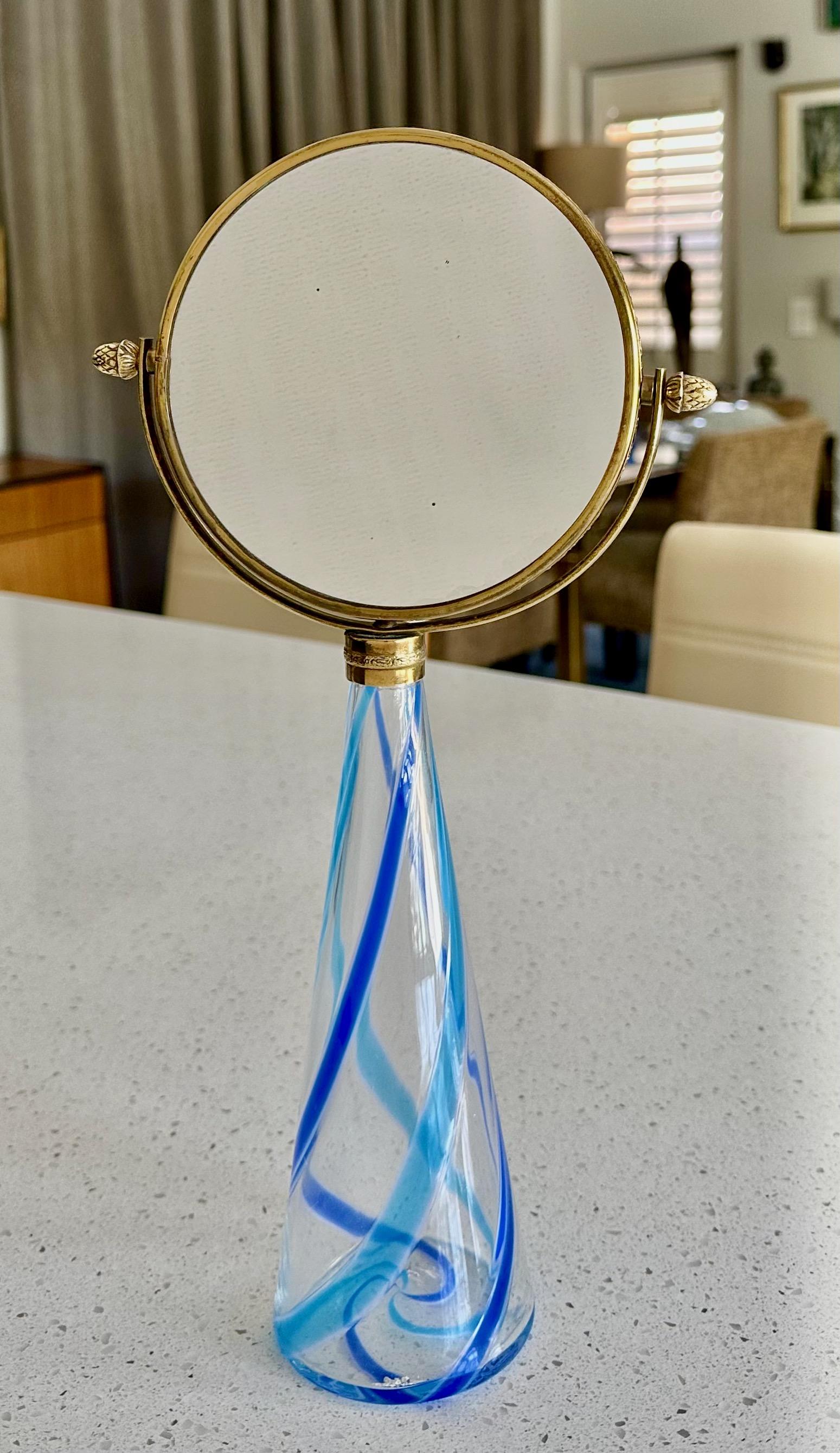 Smaller scale Murano vanity table mirror with cone shape blue and and clear stripe hand blown glass base, top is a round 2 sided swivel brass mirror. The brass has a nice warm aged patina. The mirror portion is 5