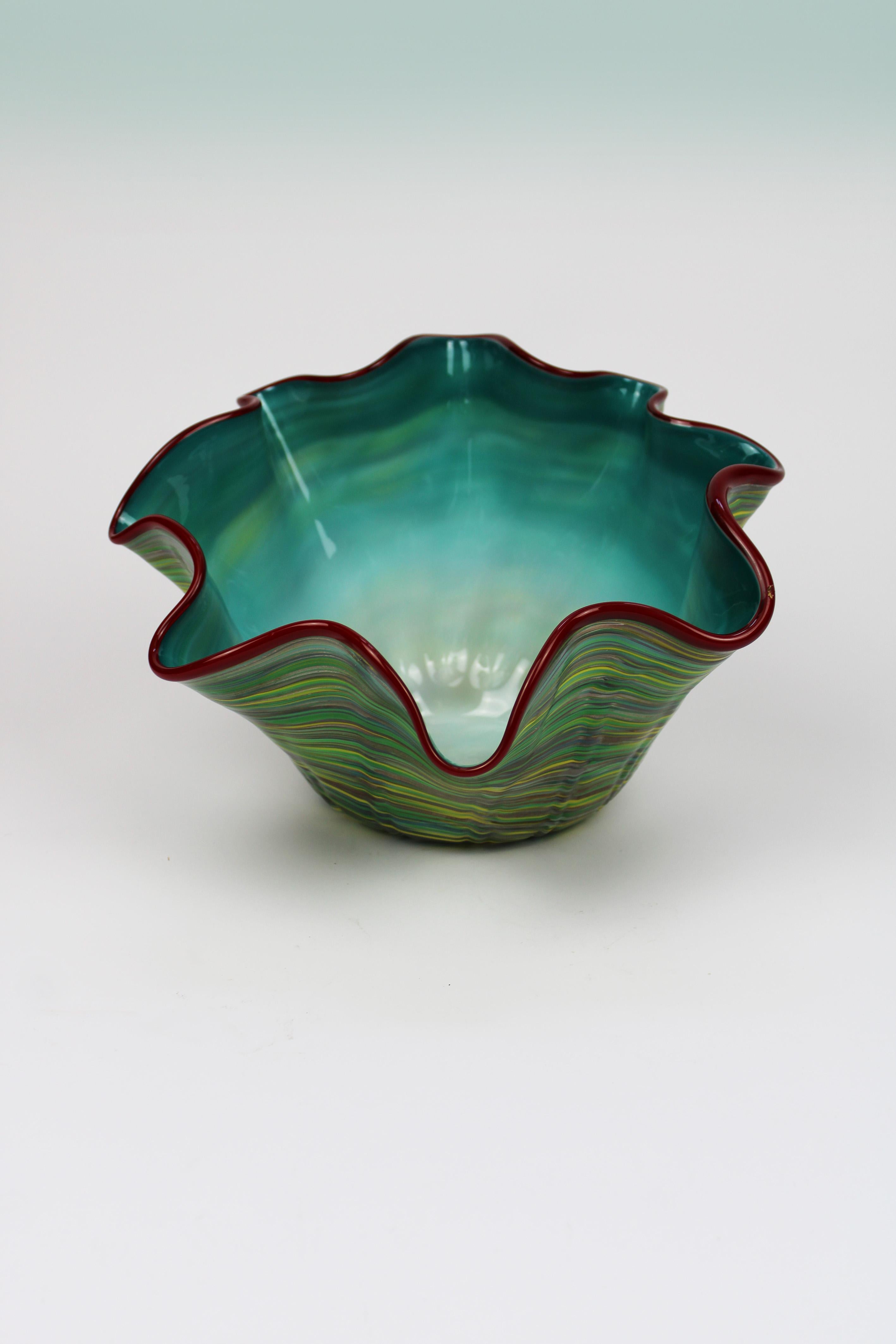 Wir stellen eine exquisite Murano-Schale vor, ein beeindruckendes Beispiel italienischer Glaskunst aus dem 20. Jahrhundert. Diese in den 1980er Jahren handgefertigte Schale hat eine organische Form, die mit lebhaften, mehrfarbigen Streifen verziert