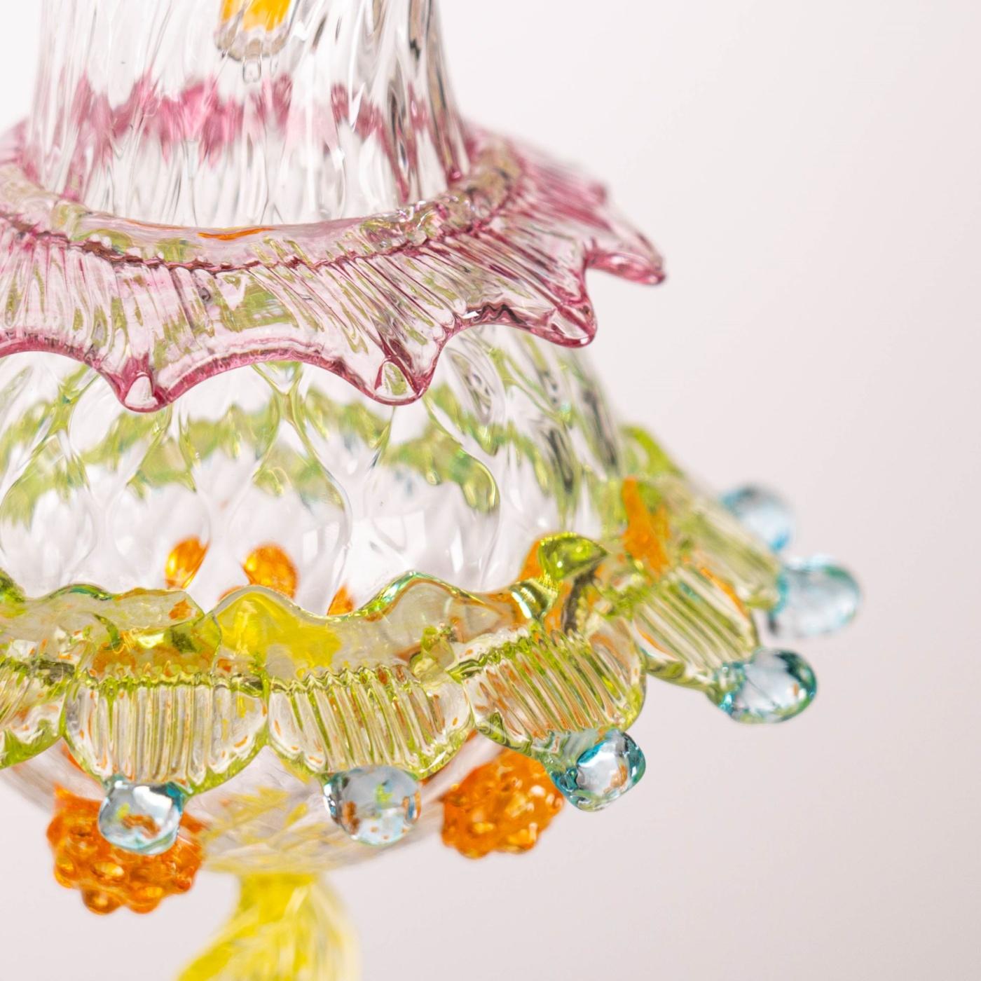 Il corpo in vetro soffiato lavorato a rigamenà è decorato con colori e forme suggestive e originali della tradizione artigianale di Murano. Il corpo centrale è circondato da decorazioni a pioggia in vetro verde acido, azzurro e pinze di rubino. La