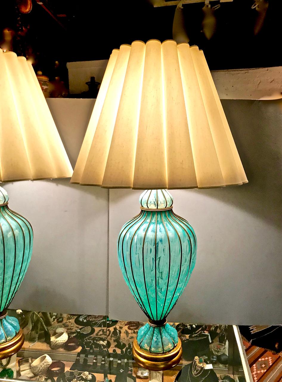 This is an unusual large pair of caged and quilted turquoise or deep aqua Murano glass lamps that dates to the late 1950s. The are in near mint condition with all elements retaining their original gilding and surface. The lamp shades and finials