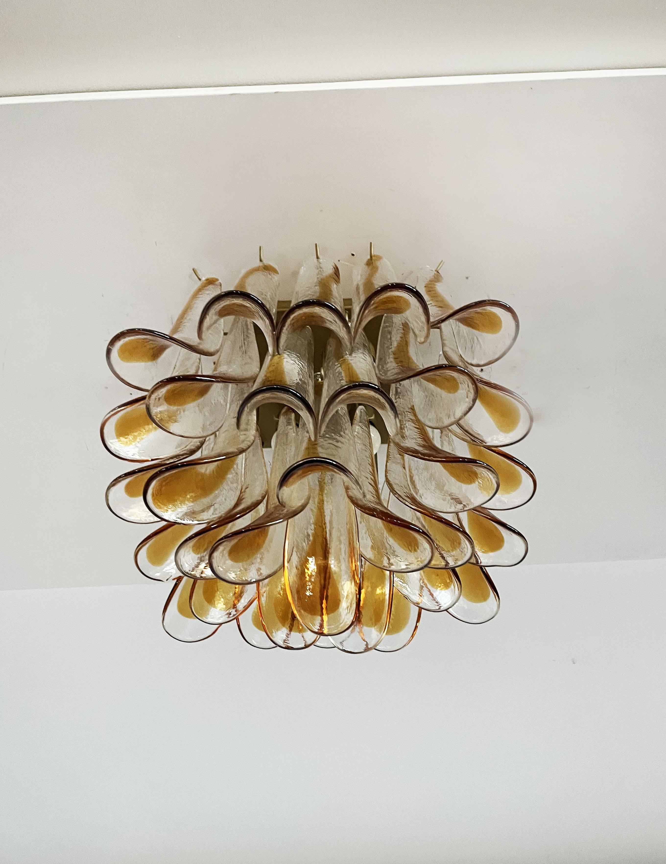 Spettacolare lampada da soffitto con 32 petali in vetro di Murano (trasparente con macchie d'ambra) in una struttura in metallo verniciato d'oro. Elegante oggetto di illuminazione.
Periodo: fine del XX secolo
Dimensioni: 19,20 pollici (50 cm) di
