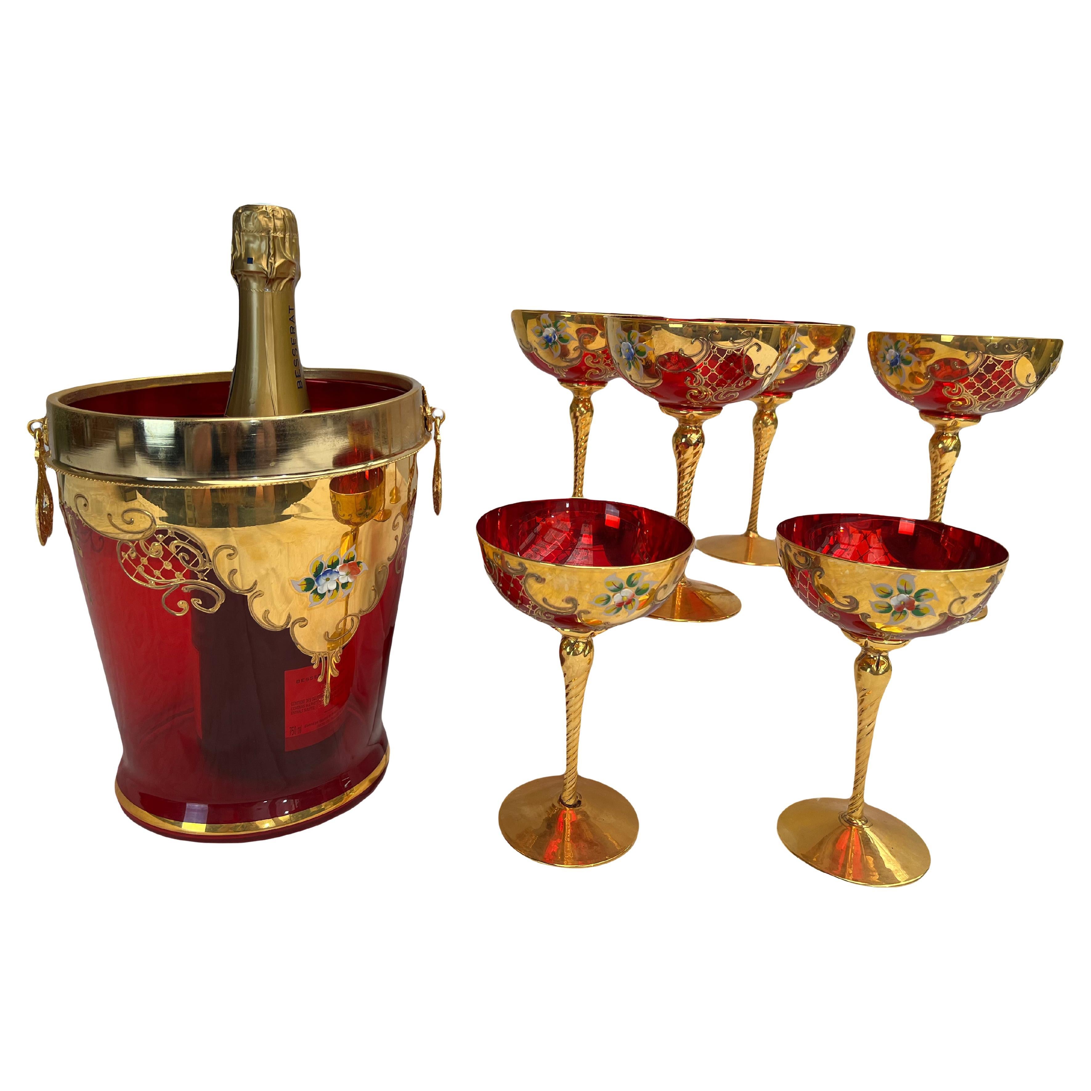 Here is a lovely champagne service composed of 6 red enameled glass flutes, accompanied by their matching champagne bucket. The glass of these flutes has a rich red hue, and their twisted stems are delicately gilded, creating an elegant contrast.