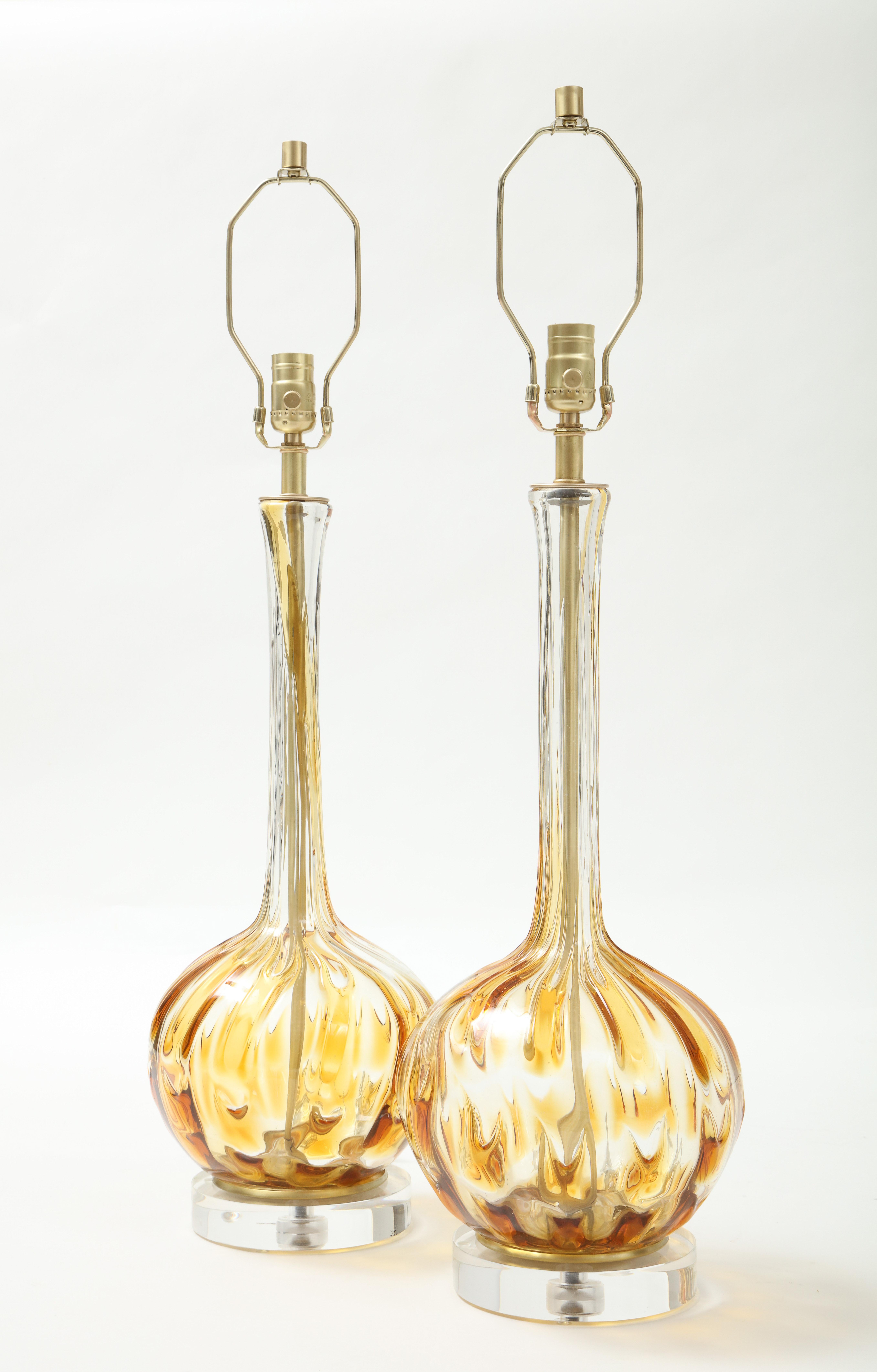 Pair of Murano genie bottle form lamps in clear Murano glass with honey colored inclusions, sitting on lucite and brass bases. Professionally rewired. 100W max.