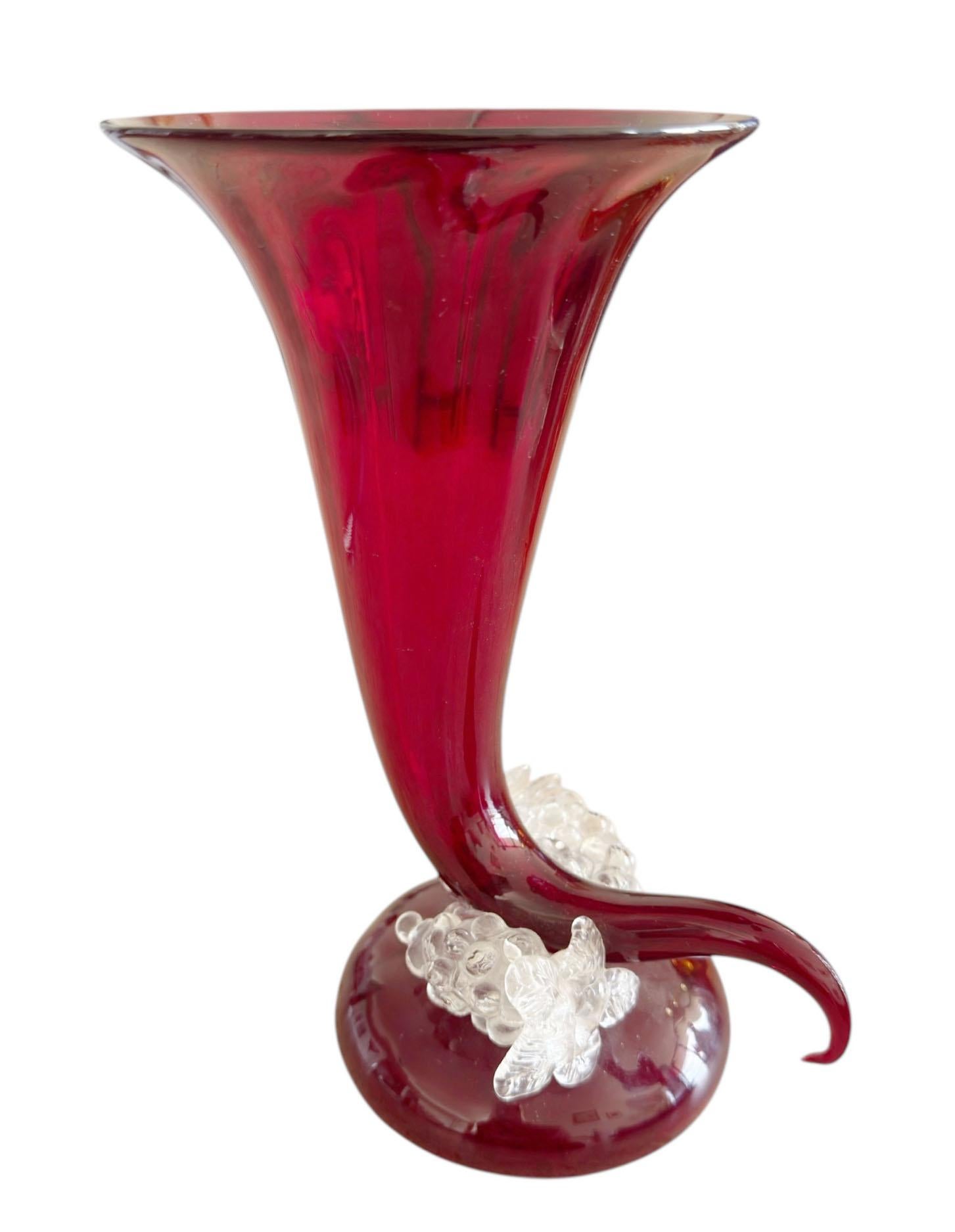 A striking example of mid century Italian artistry, this red Murano cornucopia vase is both sculptural and elegant. The vibrant ruby red horn is gracefully curled and adorned with a cascading cluster of clear glass grapes at the base. 

Made by