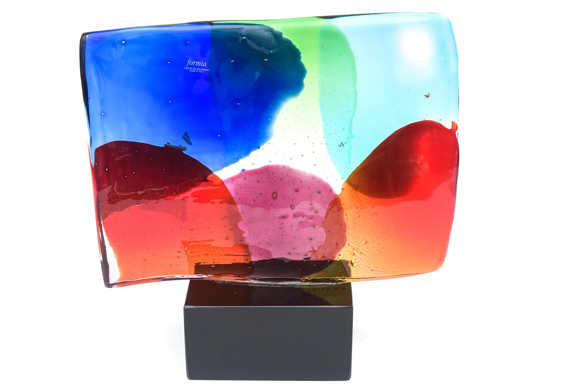 This fabulous vintage wave hand blown glass sculpture by Formia Murano was done in the 80s is like an abstract painting of luminous color patterns. It sits and is attached as was made to a black glass base. The colors range from blobs of red, sky