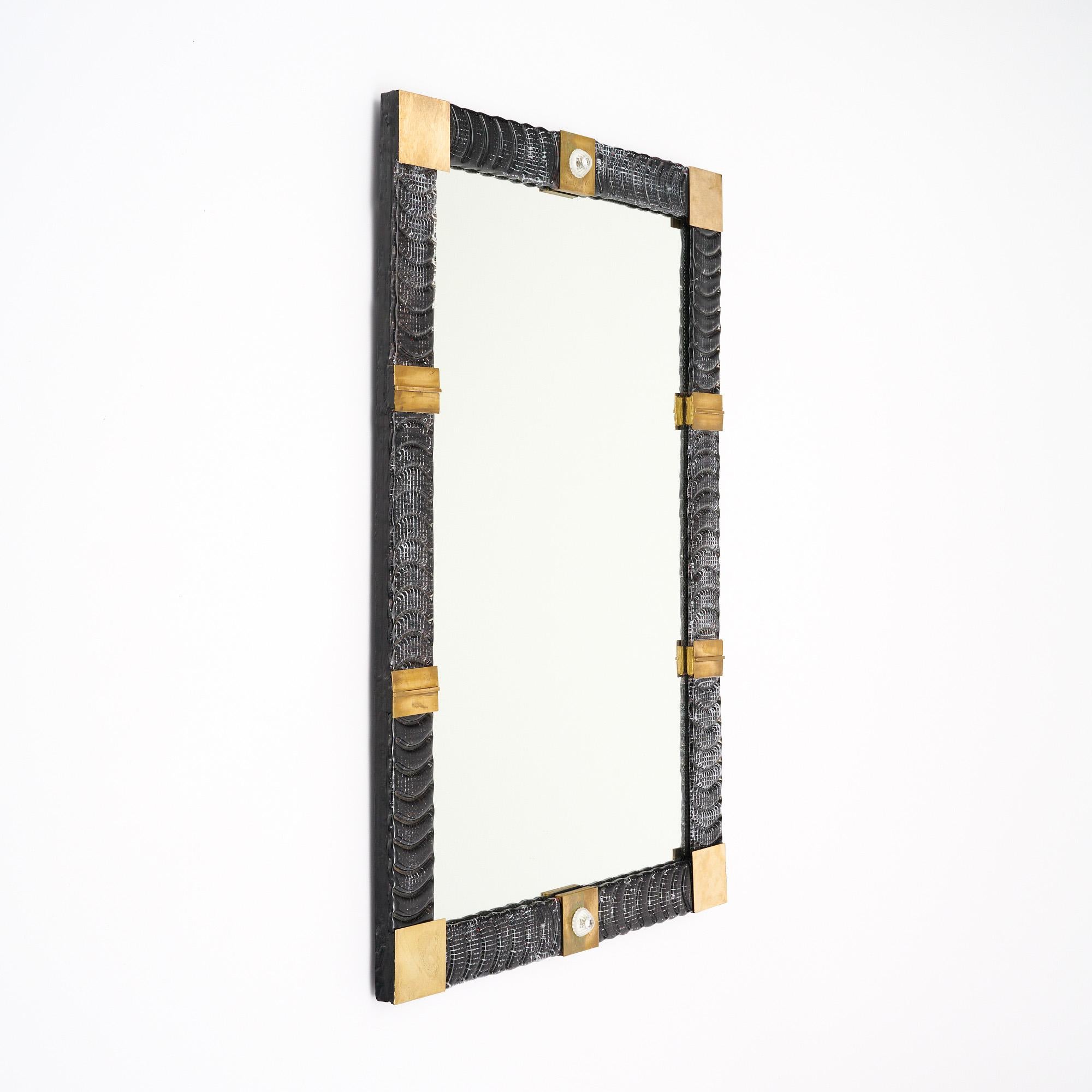 Miroir rectangulaire avec un cadre composé d'éléments en verre de Murano texturé et de laiton. Les parties en verre sont soufflées à la main dans un ton gris. Les détails en laiton sont mis en valeur par un fleuron en verre de Murano qui orne le