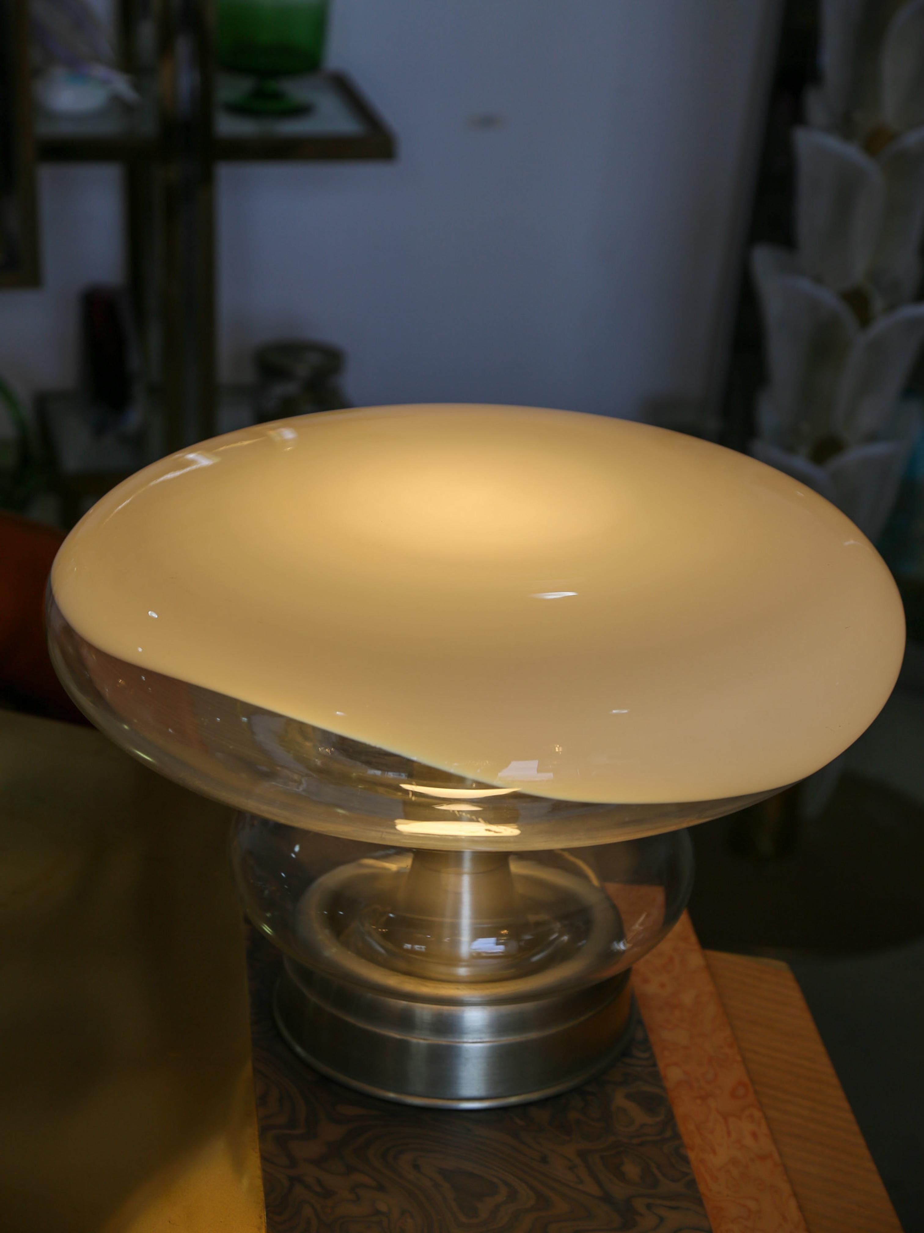 Eleva tu espacio con el sofisticado encanto de esta Lámpara de Sobremesa Roberto Pamio. Diseñada con una estética escultural, esta rara pieza vintage presenta una base de metal pulido combinada con una impresionante pantalla de cristal soplado a