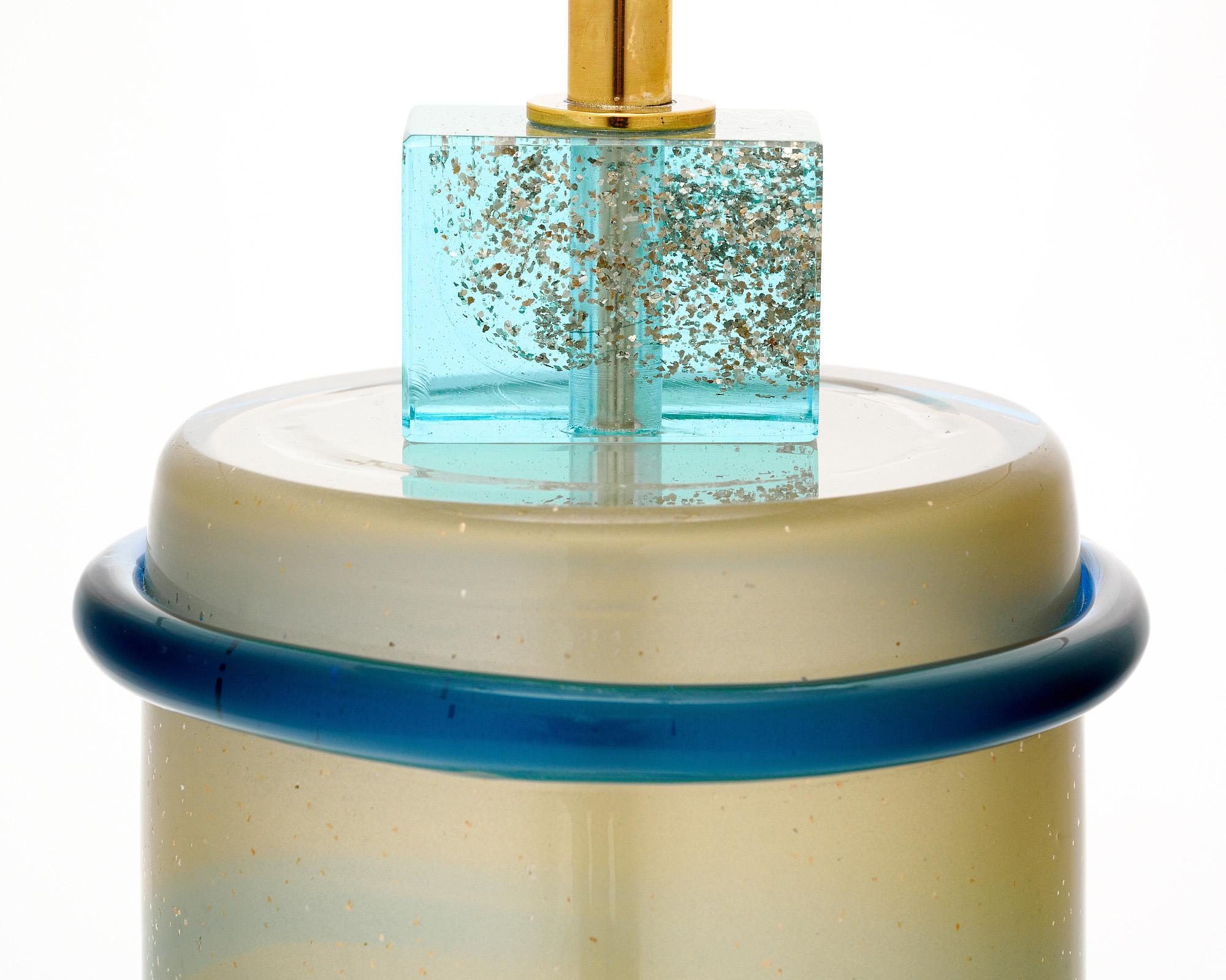 This pair of side tables is made in Murano, Italy, outside of Venice. Each has a hand-blown aqua blue cylindrical body with 23 carat gold avventurina detailing. There are darker aqua details as well. The glass is supported on a brass structure and