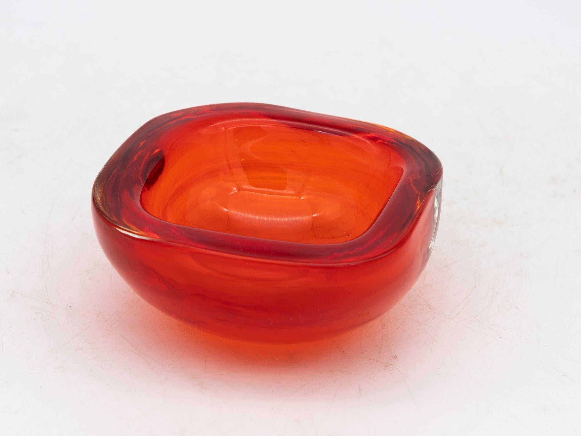 Crafted in the vibrant spirit of the 1960s, this Murano glass ashtray exudes timeless charm. With its square shape and gently rounded corners, the thick glass construction boasts both sturdiness and elegance. The color palette, a vibrant orange red,