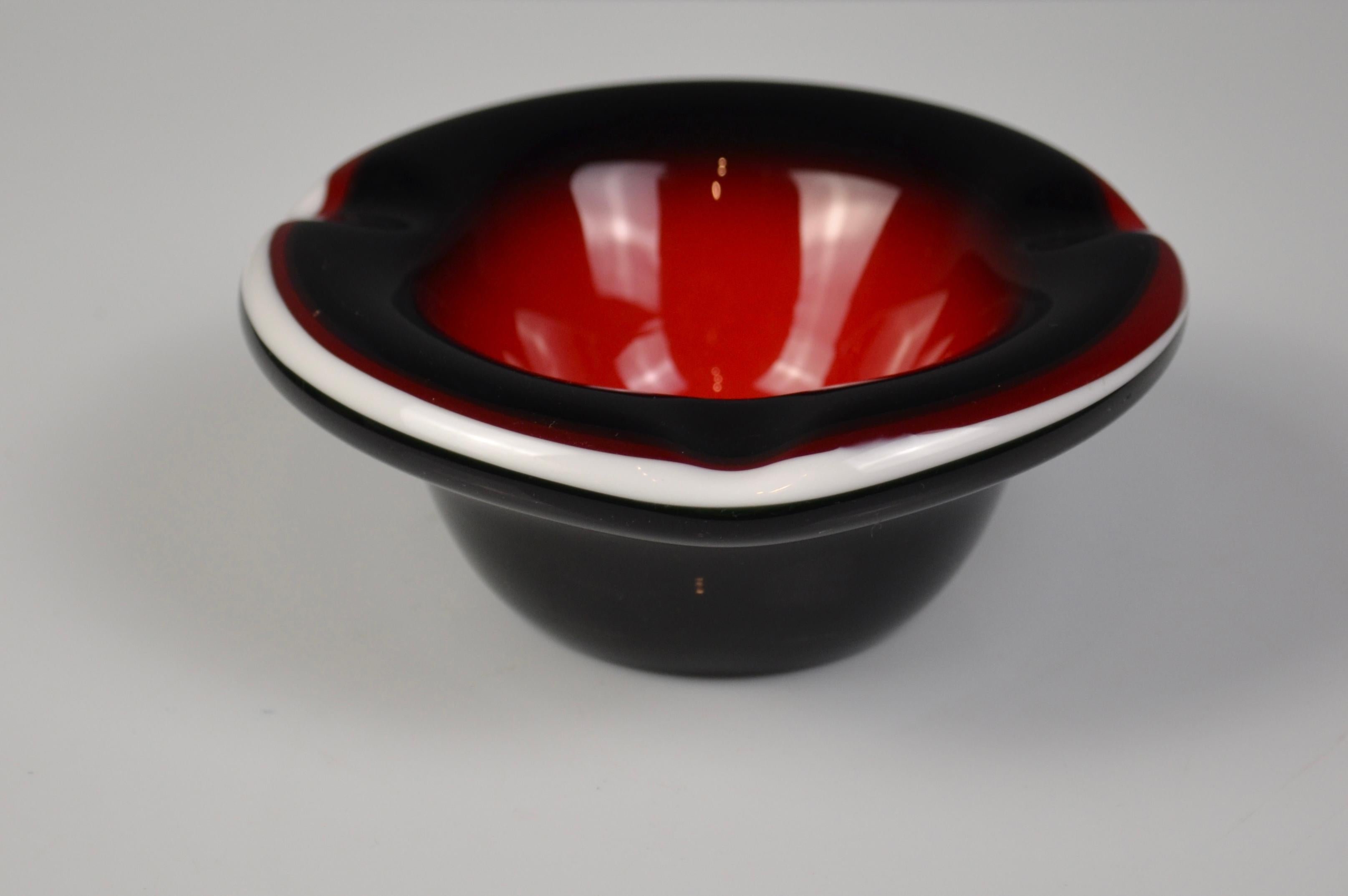 Elegante posacenere in vetro di Murano in vetro rosso, nero e bianco.
Questo pezzo scultoreo soffiato a mano combina vividi contrasti di colore e linee organiche morbide, tipiche dell'artigianato di metà secolo.
La sua sorprendente combinazione di