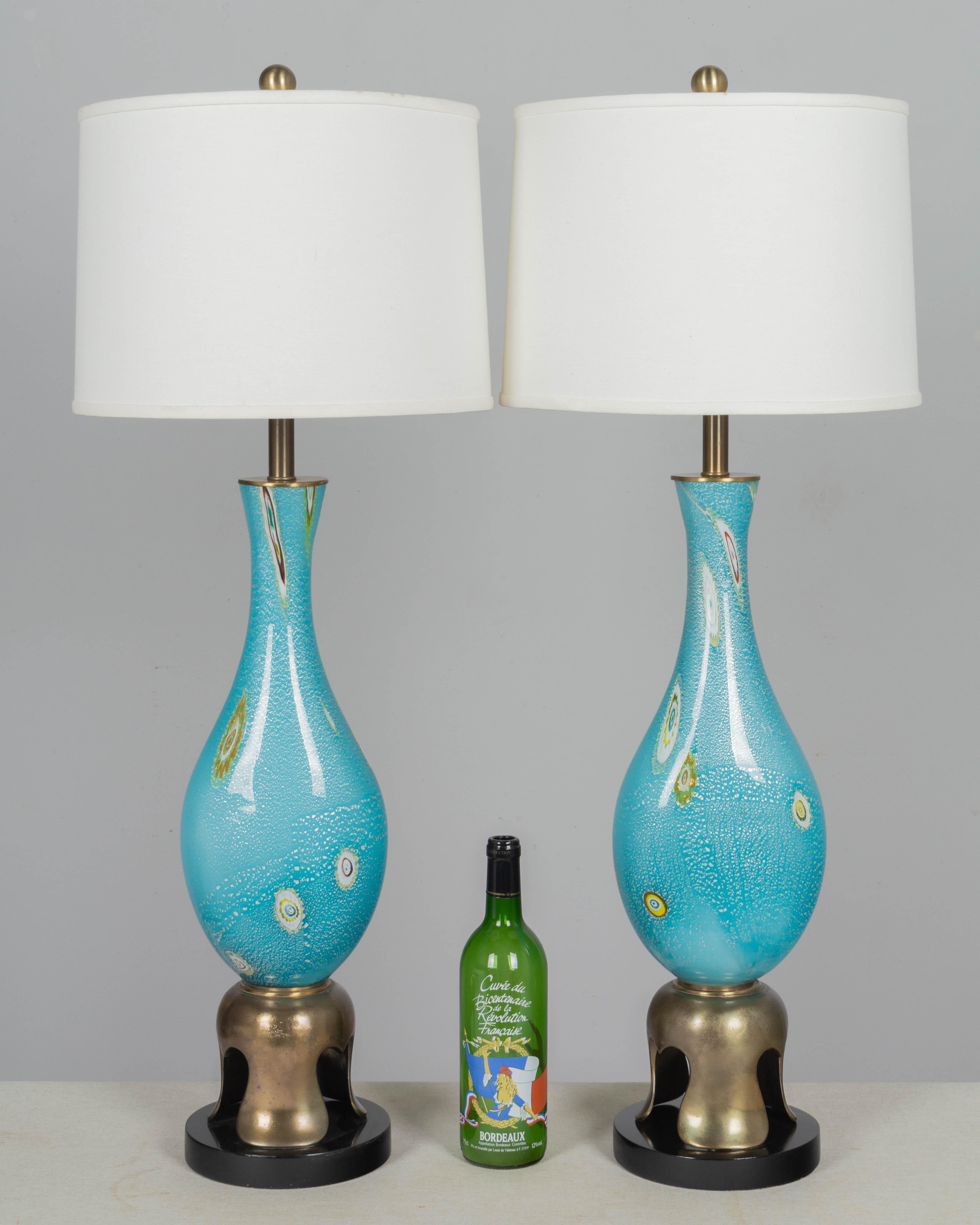 A pair of midcentury Murano art glass table lamps by Barovier & Toso. Hand blown aqua blue glass with colorful murrines and silver foil. Original brass tone cast brass and black painted wood bases, in the style of James Mont. Red foil label on one