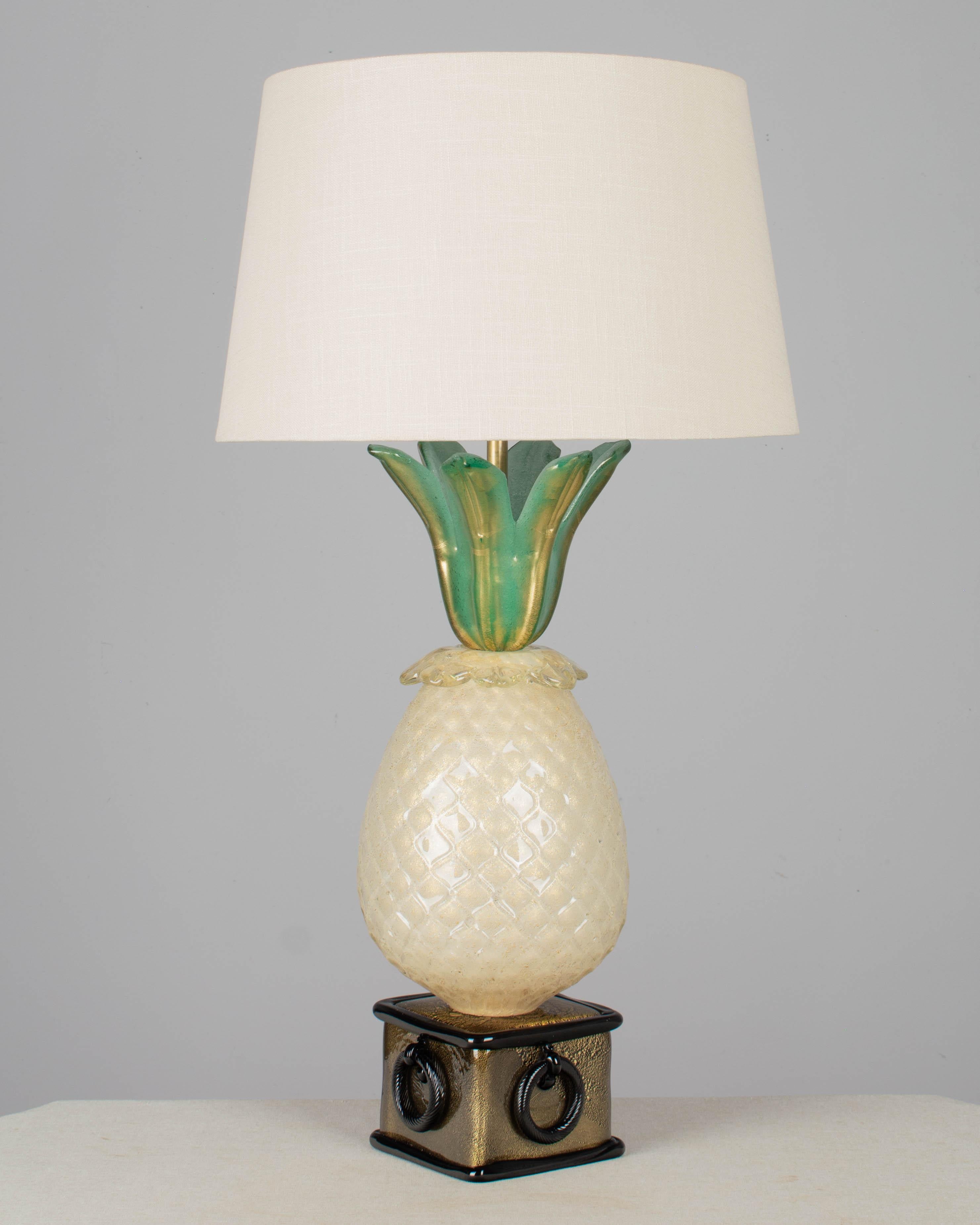 A Mid Century Murano glass pineapple form lamp by Barovier & Toso. In three parts: square black base with ring form details, large textured pineapple, and green leaves, all with gold inclusions. An impressive large statement lamp for an entryway or