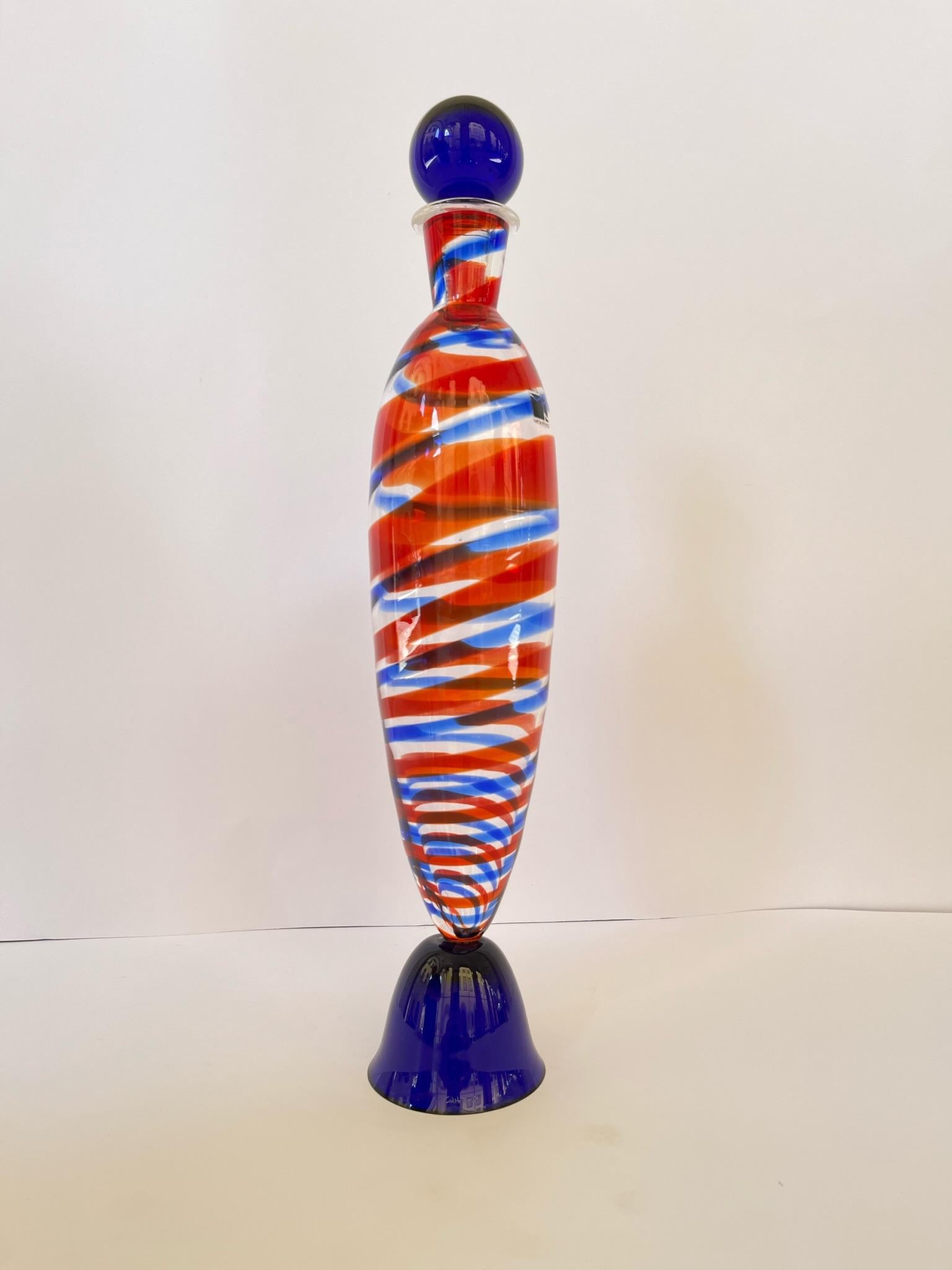 Bottle in Murano glass signed Carlo Moretti.
Sketch brushstroke in two colorations, blue and red complete of cork and label of the epoch 1980.
The base and the cap are in blue color, and the body of the bottle is a transparent base with a blue
