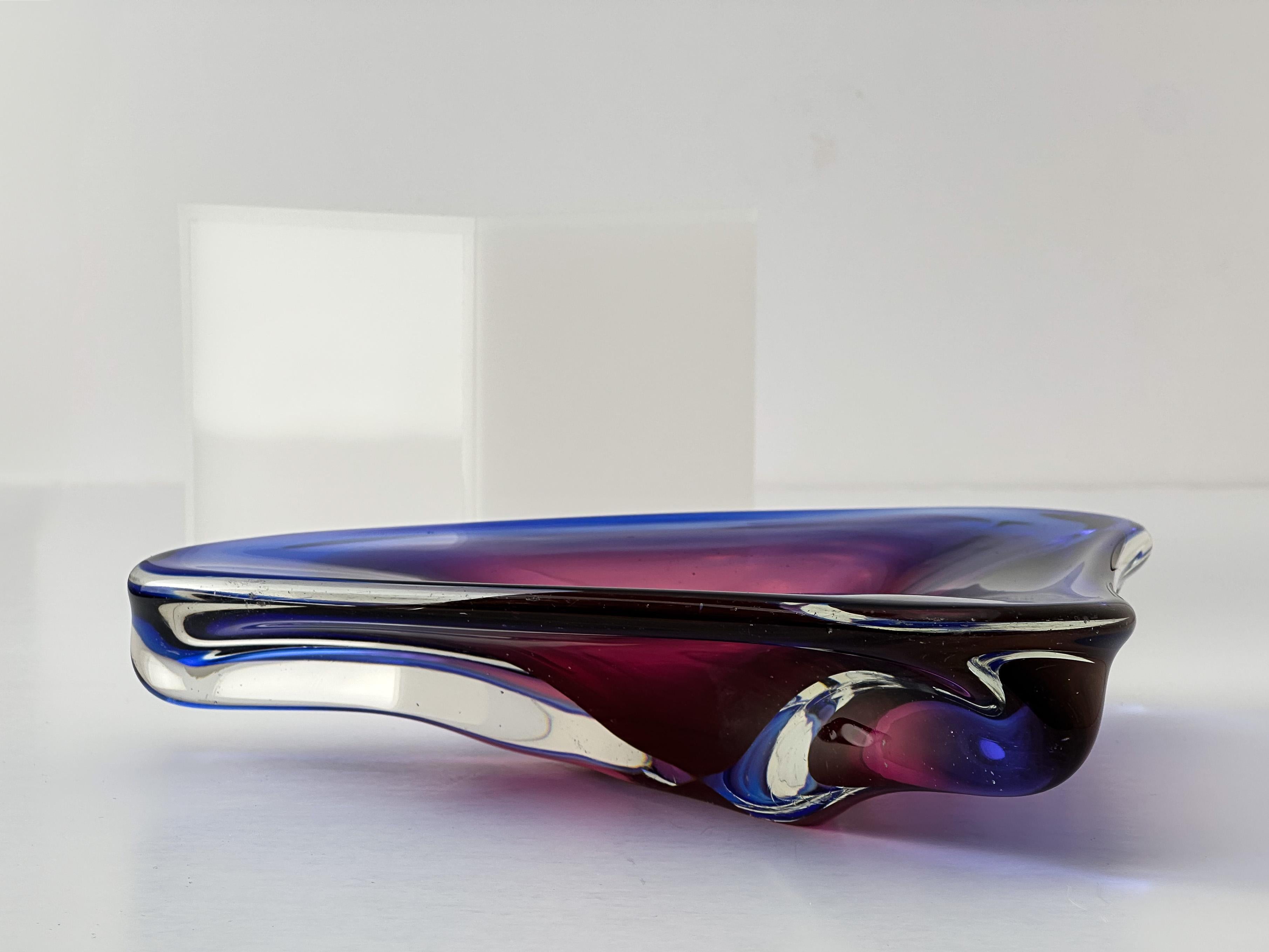 Eine auffällige dreieckige Schale aus Murano-Glas, die Oball zugeschrieben wird, ca. 1970er Jahre.

Diese Vintage-Schale aus einer leuchtenden Mischung aus blauem und rosafarbenem Murano-Glas ist ein typisches Beispiel für die Kunstfertigkeit der