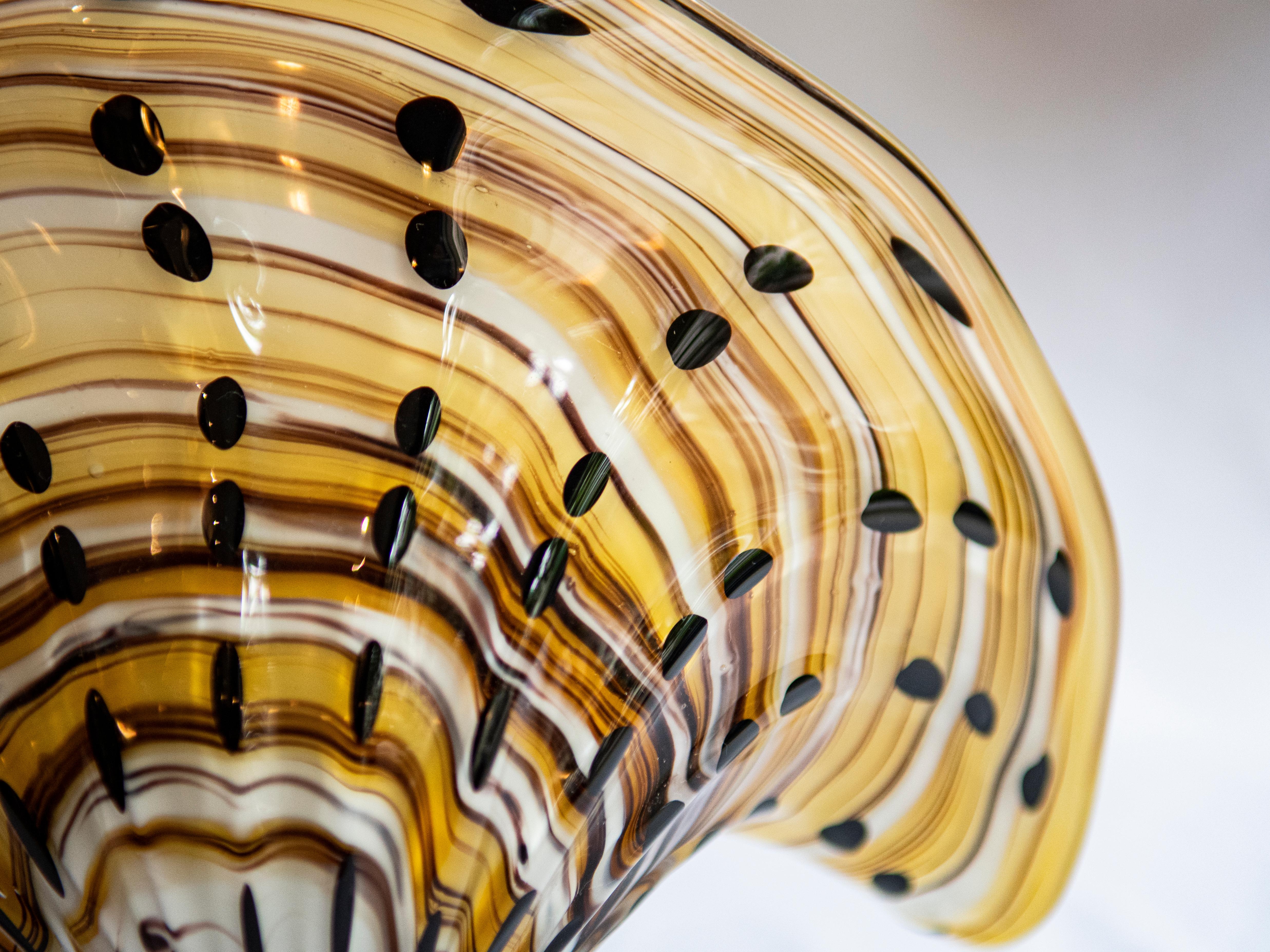Admirez la beauté exquise de ce vase en verre de Murano, gracieusement sculpté en forme d'éventail. Son design enchanteur est rehaussé par une dégradation des couleurs hypnotique, passant de teintes vibrantes à des nuances délicates à chaque courbe