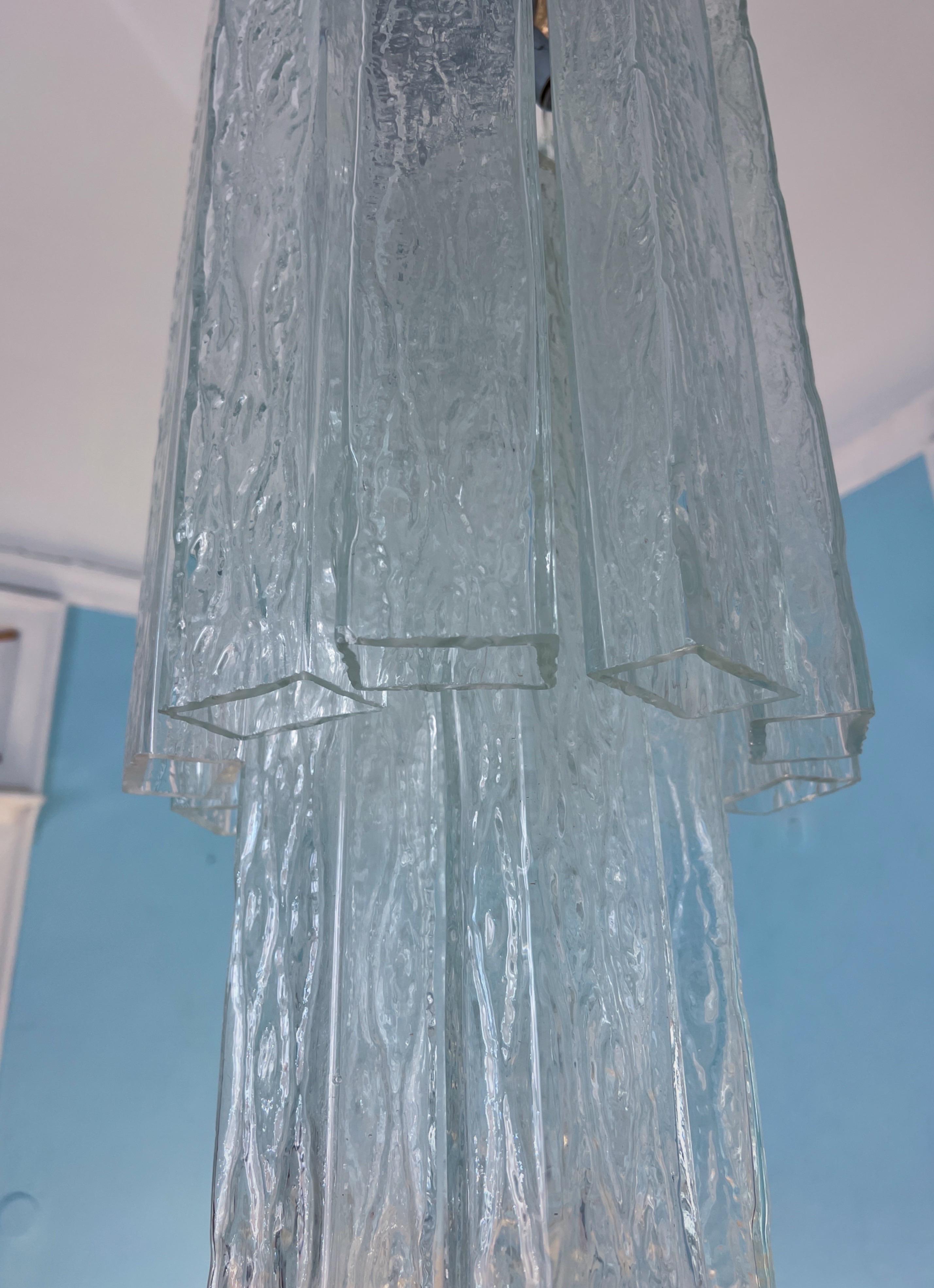 Conçu par Toni Zuccheri pour Eleg dans les années 1970, ce lustre est un parfait exemple d'élégance minimaliste associée à un design saisissant. Sa forme allongée et élancée en fait un choix idéal pour un couloir ou une entrée, où ses lignes épurées