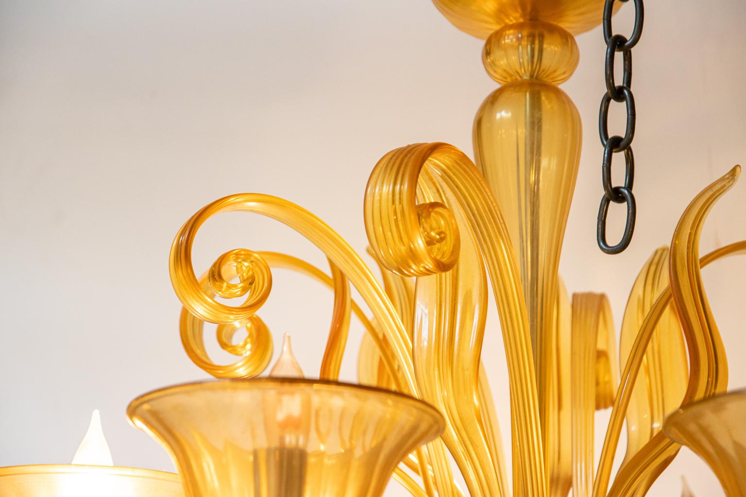Italian murano glass chandelier in amber toned glass with large cup shaped bobeches. The chandelier is also constructed with scrolled accents and a large pendant bulb shaped finial at the base. Please note of wear consistent with age.