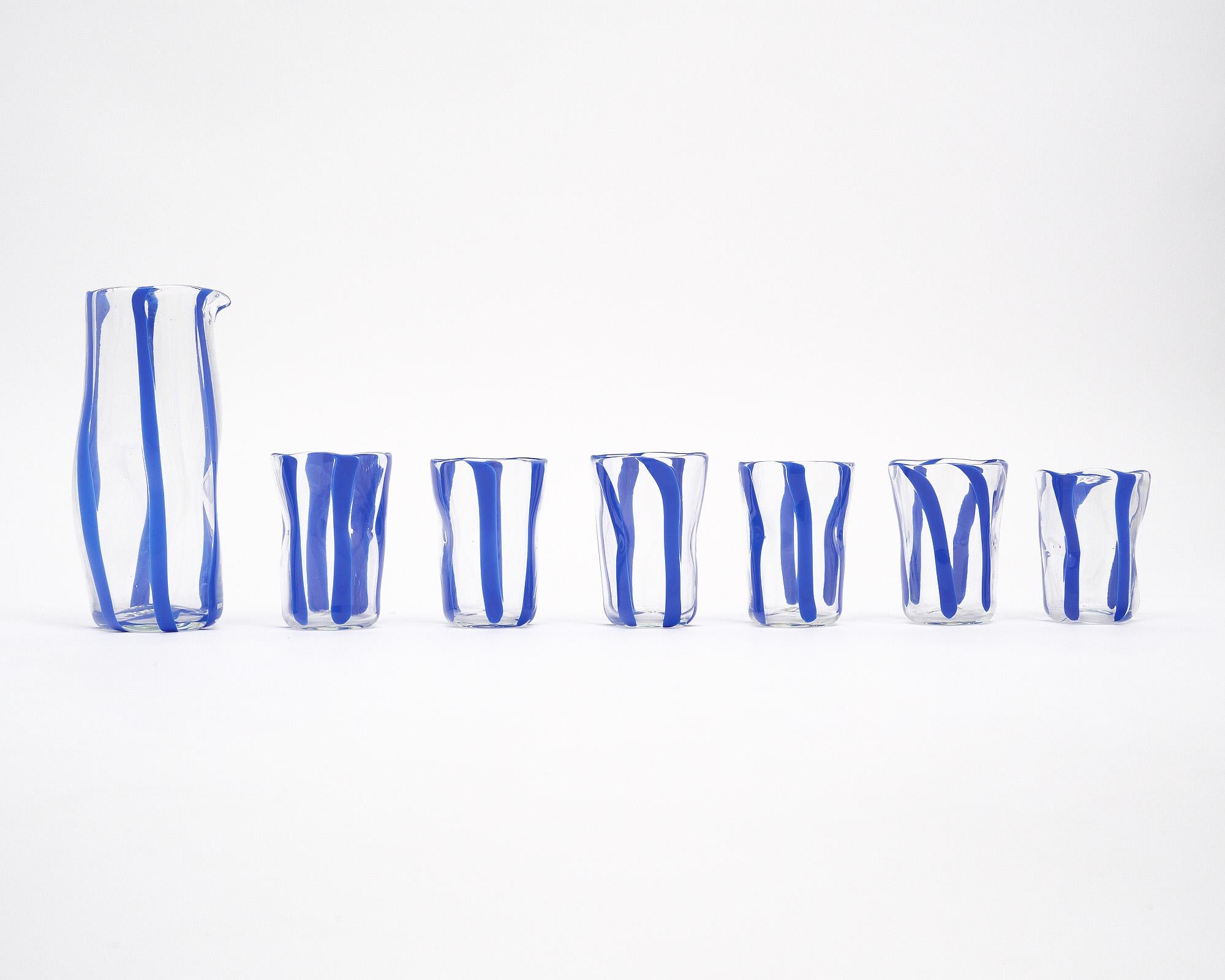 Set of six Murano glass cups and matching carafe. This set is made entirely of hand-blown glass on the island of Murano outside of Venice, Italy. They feature a transparent glass with cobalt blue stripes. We love the organic shapes and feel of this