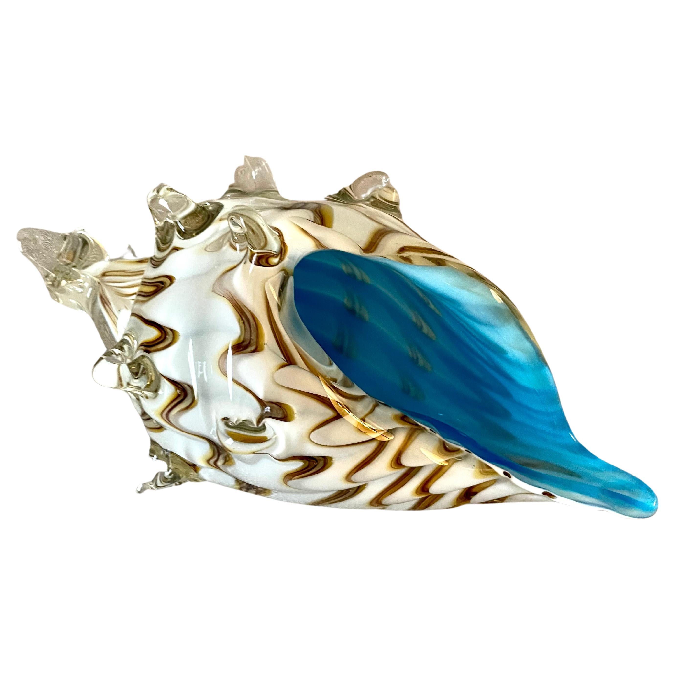 A conch shell of Murano Glass. The Italian hand crafted shell has a lovely color pattern with a dynamic interior blue accent. A wonderful decorative piece for any cocktail table, shelf or side table. Perfectly suited for the home near the sea or