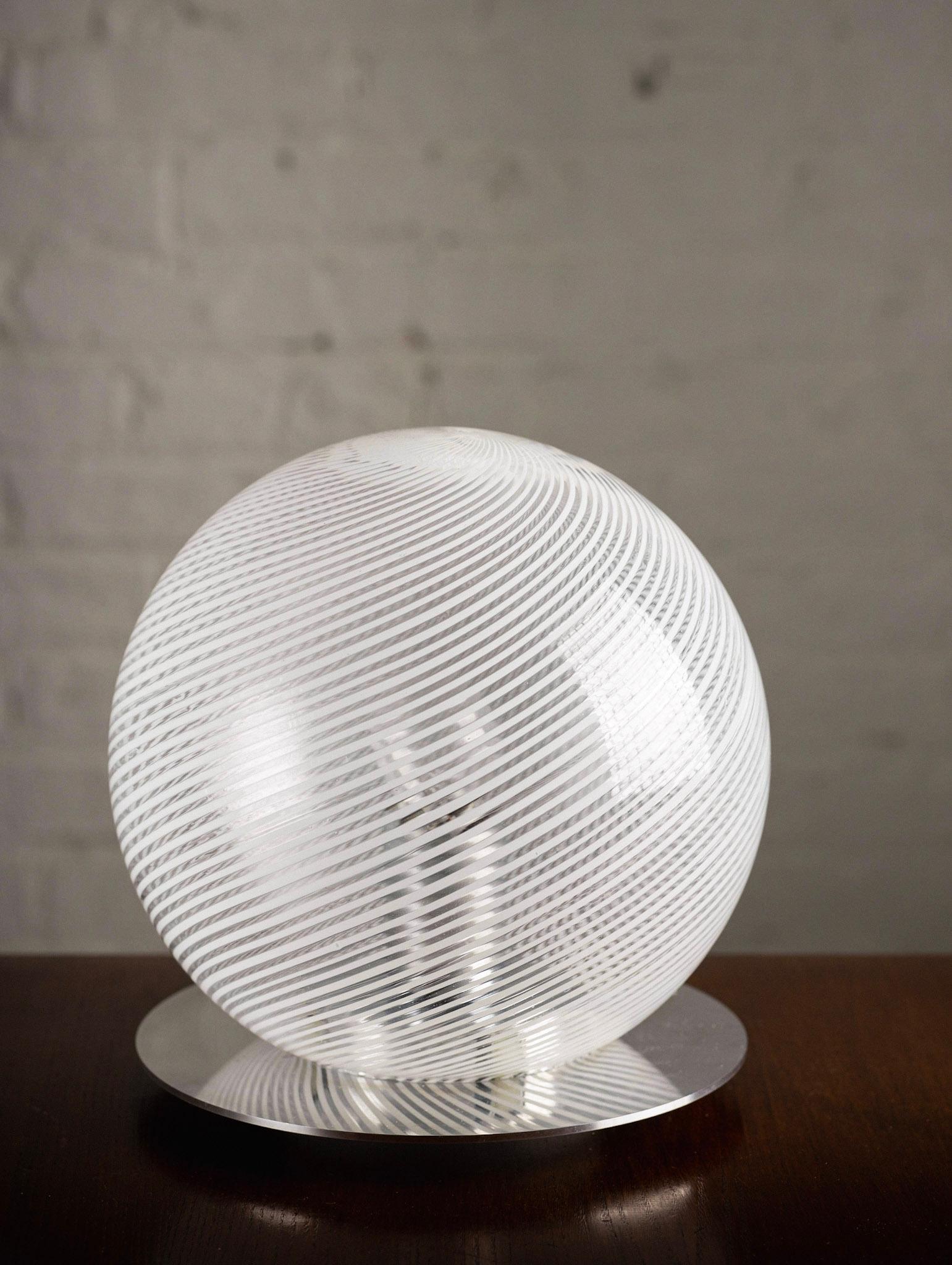 Mid century Murano glass table lamp by Paolo Venini. Transparent and white spiral glass orb on a chrome disc base. Sold individually.
Orb measures 9” in diameter.
