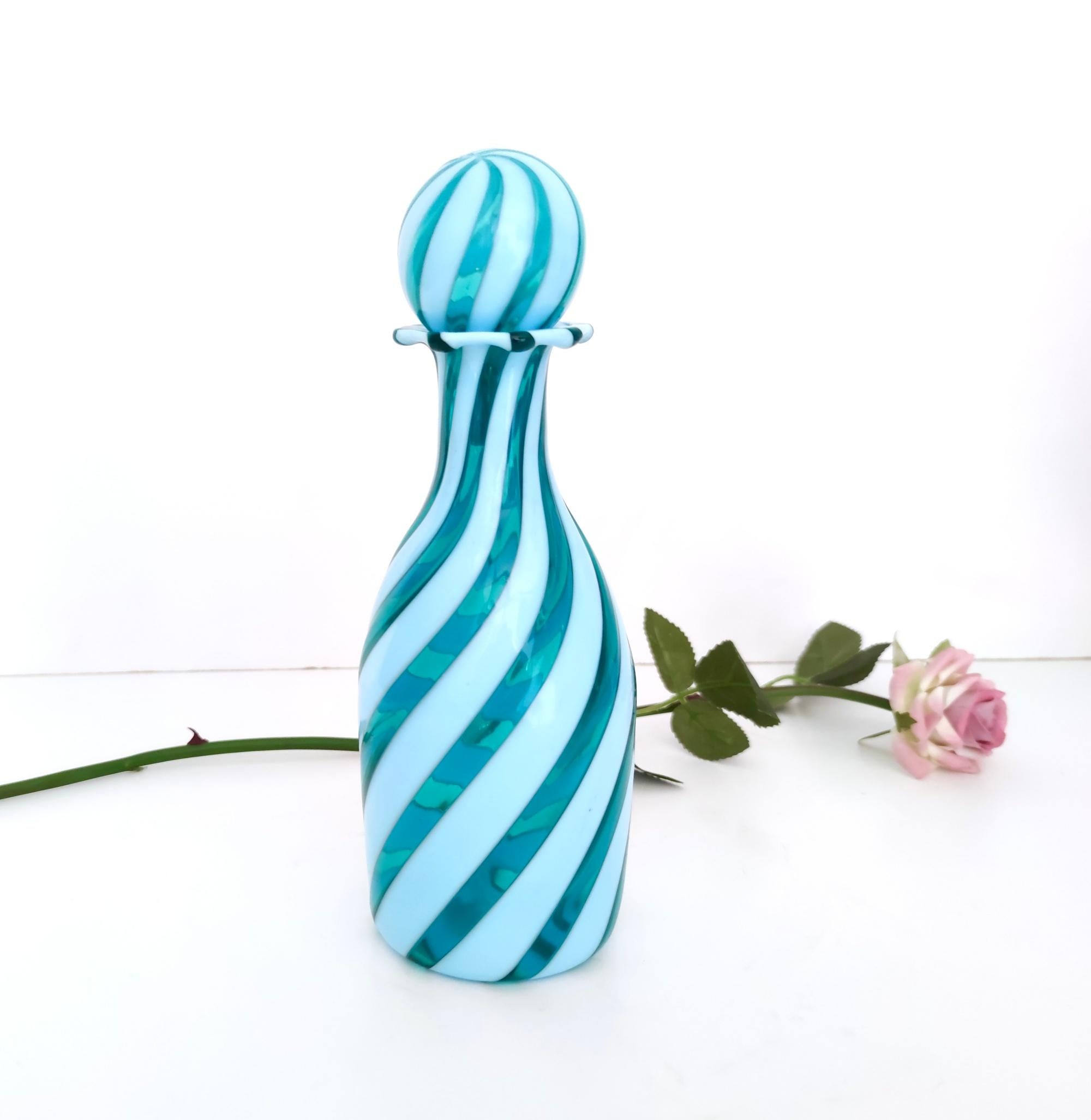 Made in Italy, 1950s.
This decanter is made in Murano glass and features teal and white canes.
It has particles of coal that are included in the glass due to its process of manufacturing: as a matter of fact in 1950s in Murano, wood-burning ovens